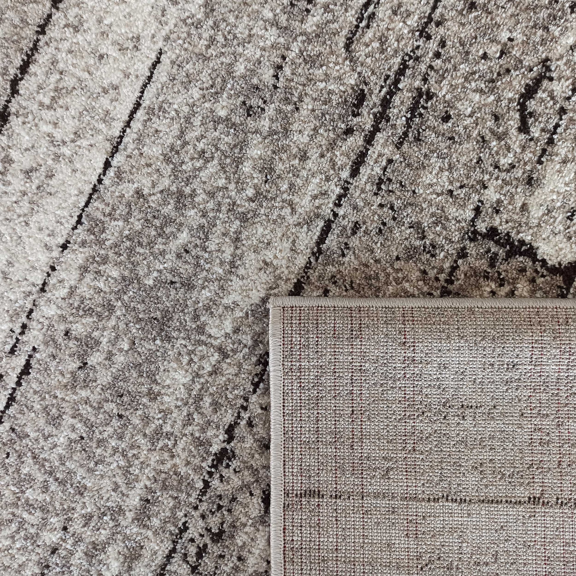 Gros plan sur un tapis texturé beige et gris avec des motifs abstraits. Son envers clair et tissé est visible
