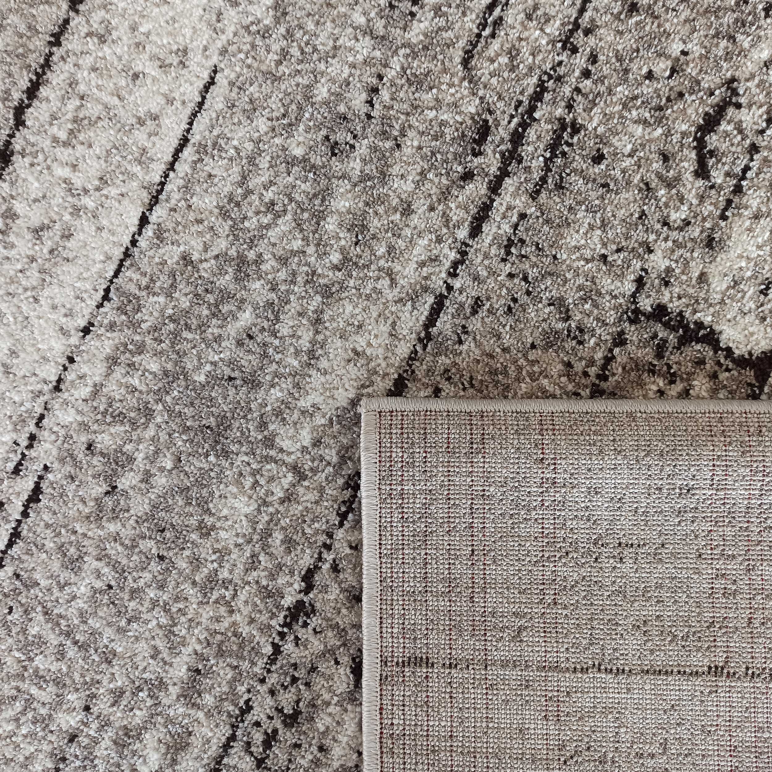 Gros plan sur un tapis texturé beige et gris avec des motifs abstraits. Son envers clair et tissé est visible