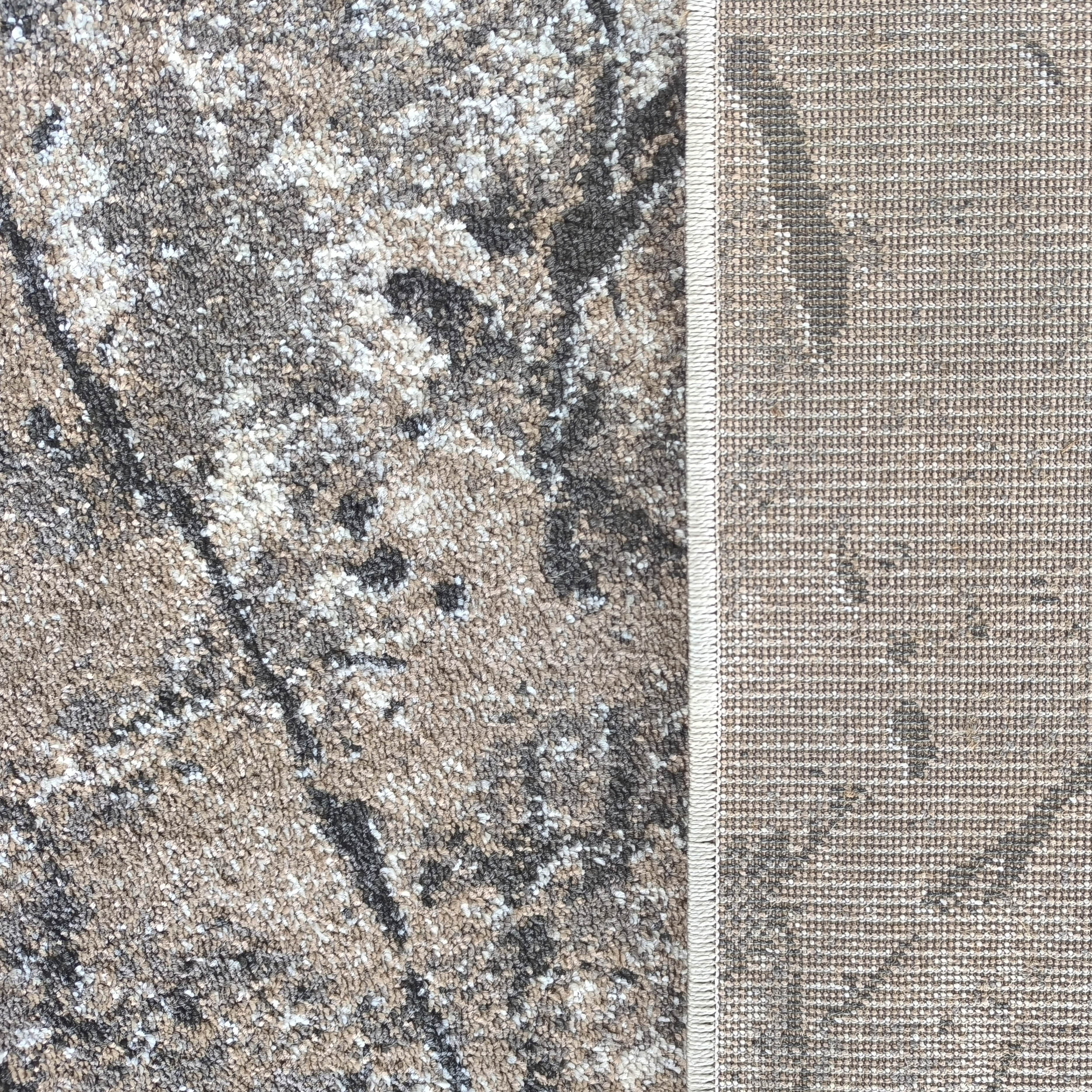 Tapis moderne aux mèches courtes marron, grises et blanches formant un motif abstrait, avec l'envers tissé beige visible sur le côté