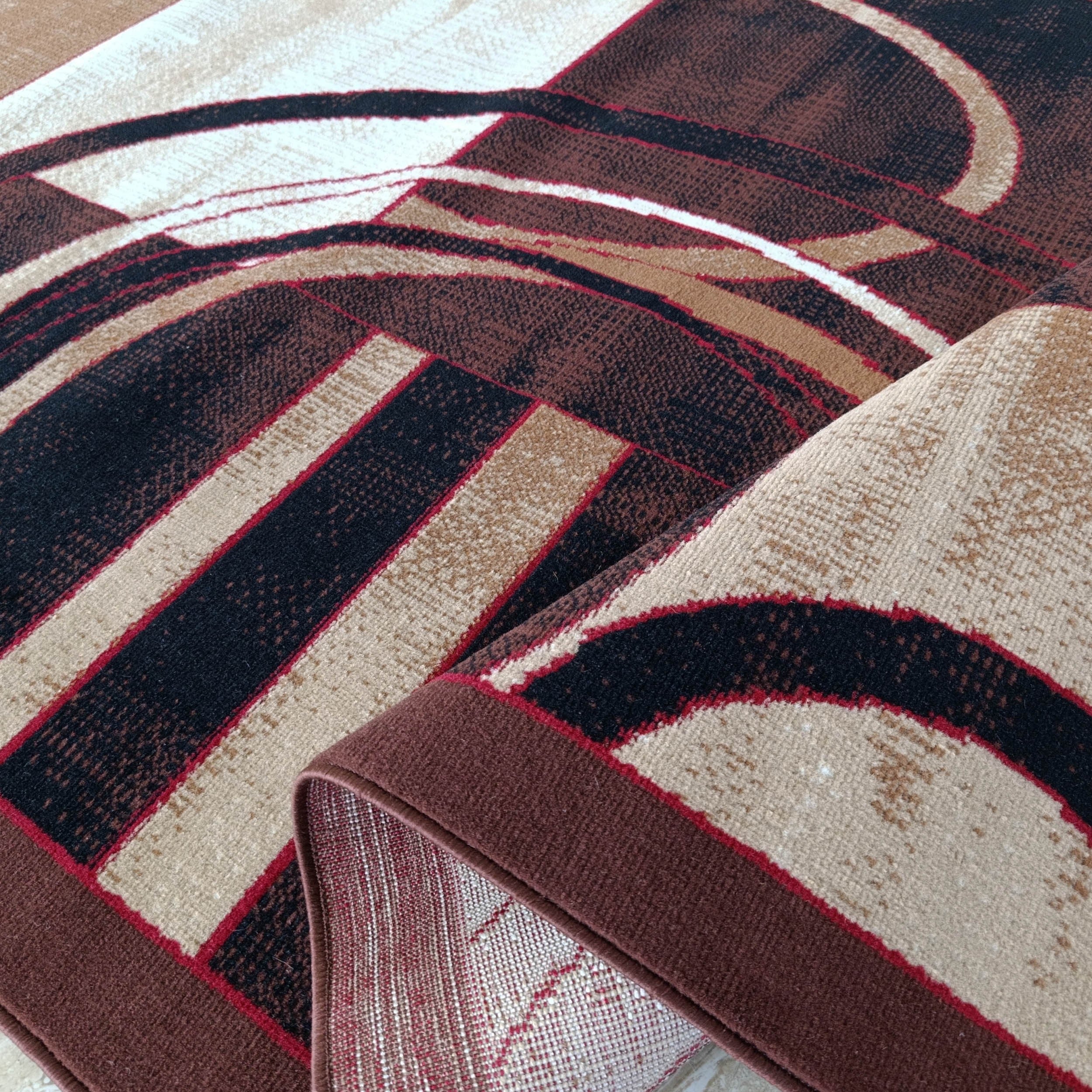 Un tapis roulé exhibe son motif abstrait de lignes et blocs beige, blanc, marron foncé, noir et rouge, l'envers tissé