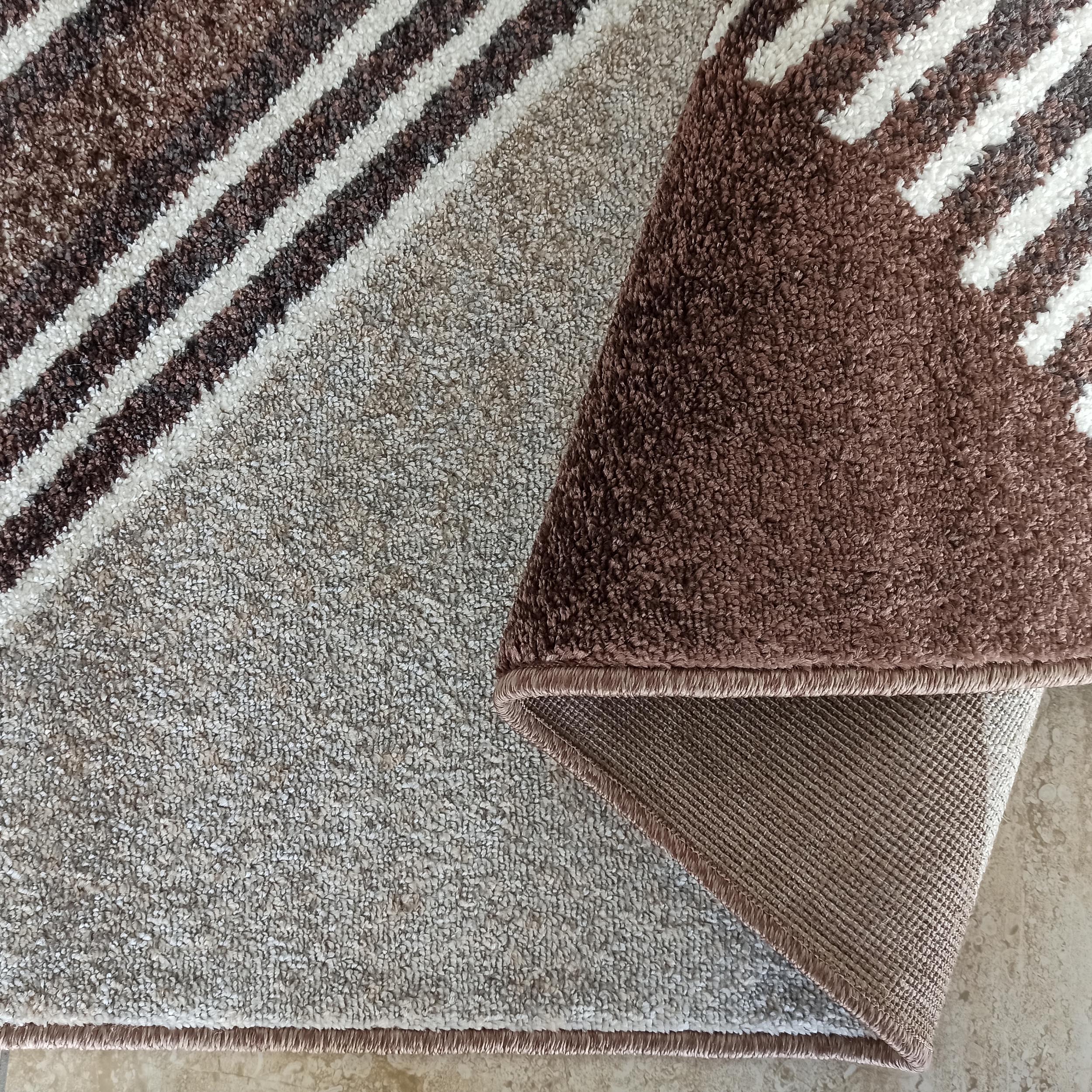 Tapis moelleux aux motifs de rayures diagonales marron foncé, blanches et beiges. Une partie est roulée, révélant son envers tissé et sa bordure