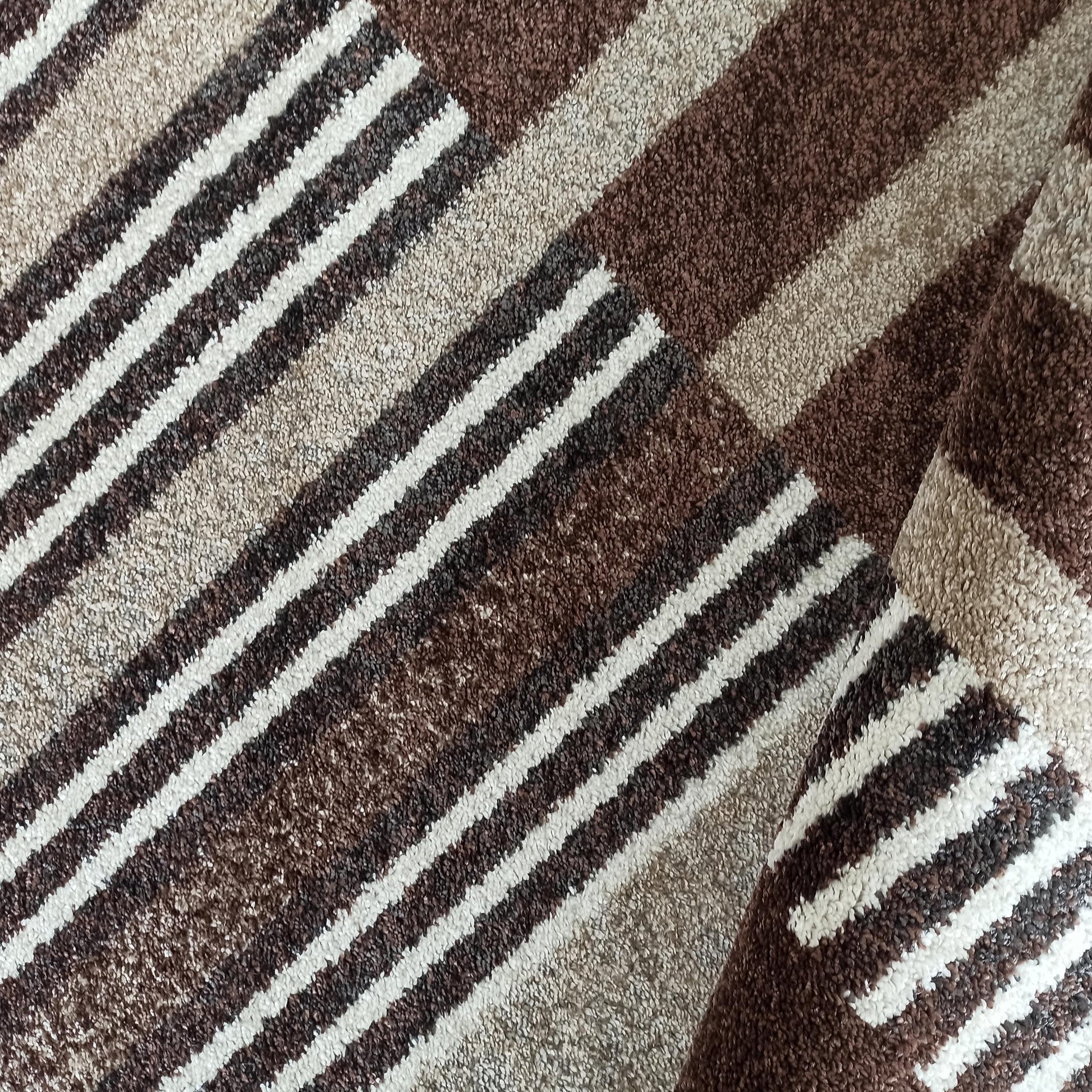 Tapis bouclé aux motifs de larges rayures diagonales et blocs géométriques en marron, beige et blanc, une partie roulée