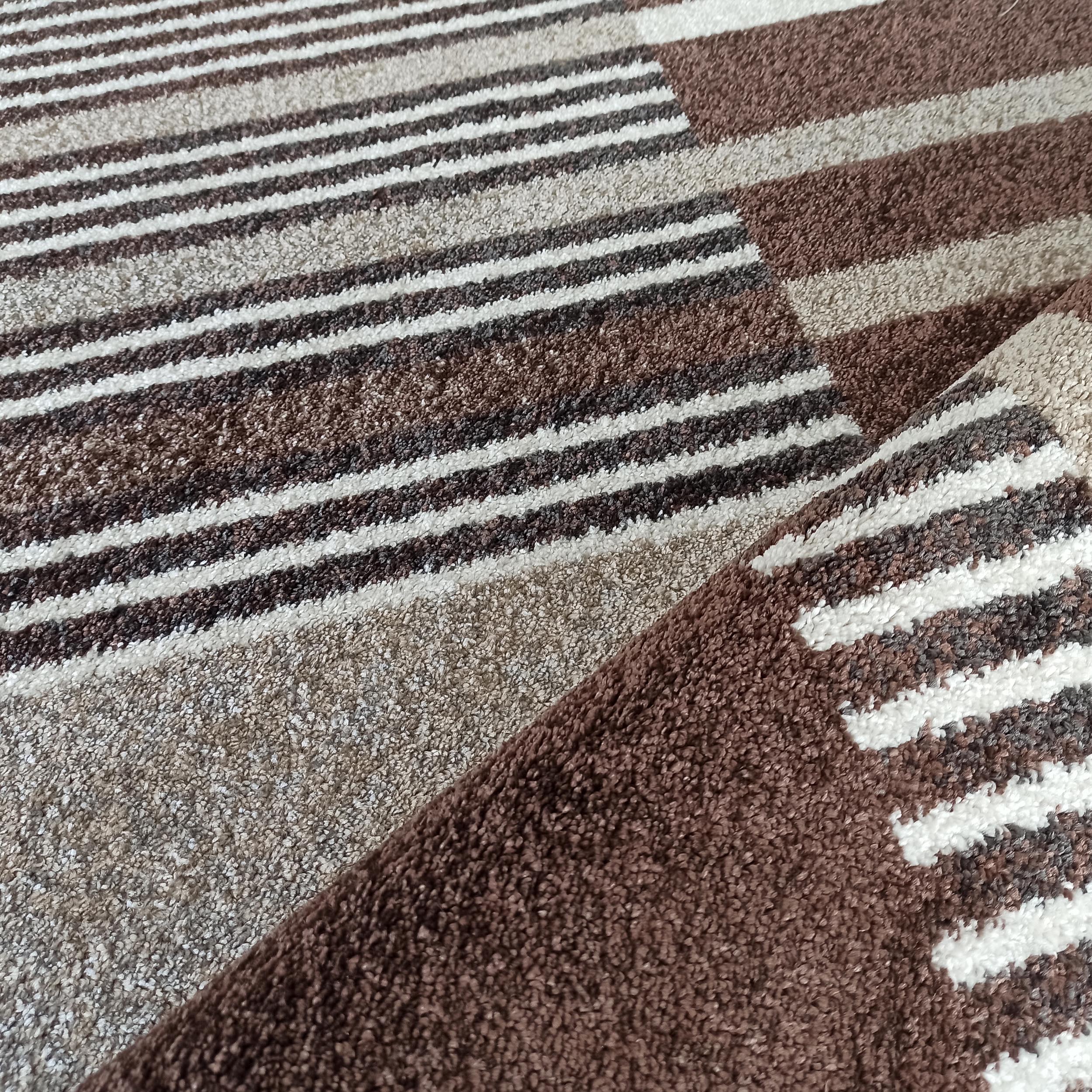 Tapis texturé à rayures marron, beiges et blanches, avec une section pliée révélant sa densité