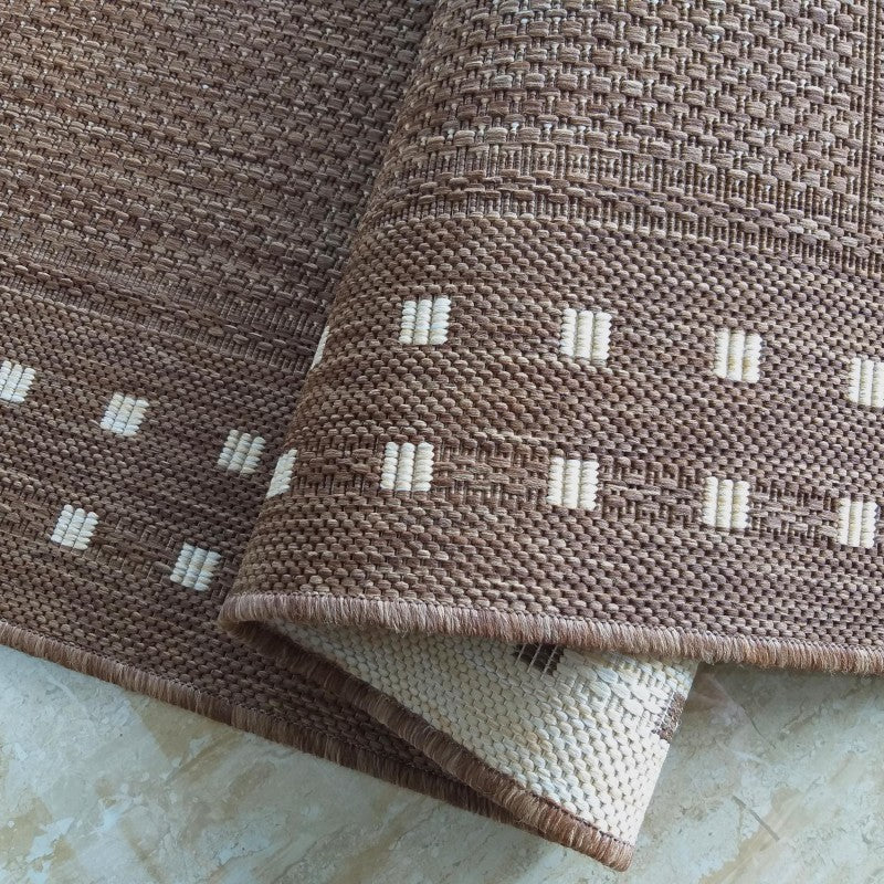 Tapis marron en matière tressée avec des motifs de barres écrues. Un coin est roulé, laissant voir l'envers clair