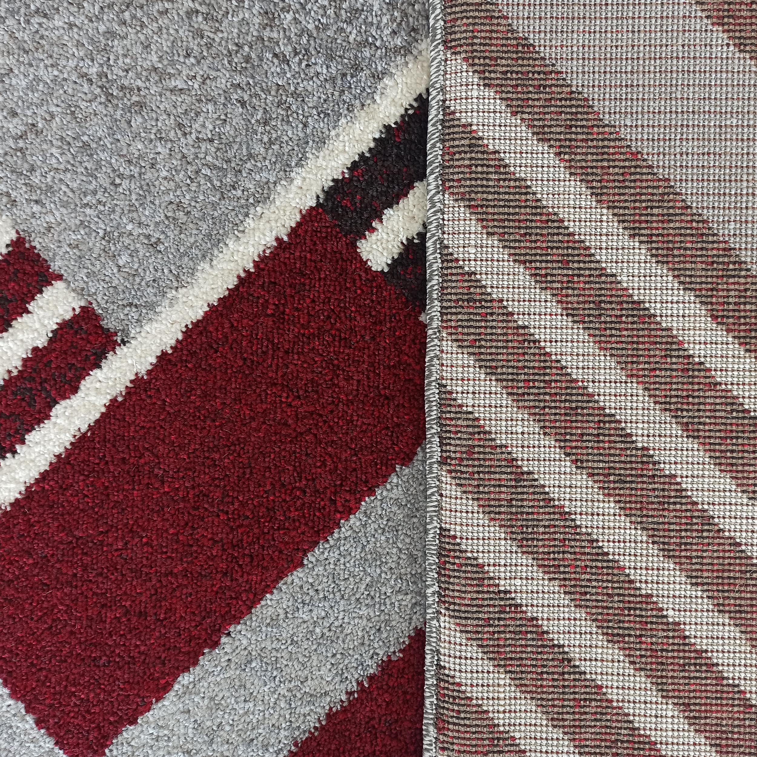 Tapis à poils longs avec des motifs géométriques diagonaux gris, rouges, blancs et noirs, montrant son dos tissé en beige et rouge