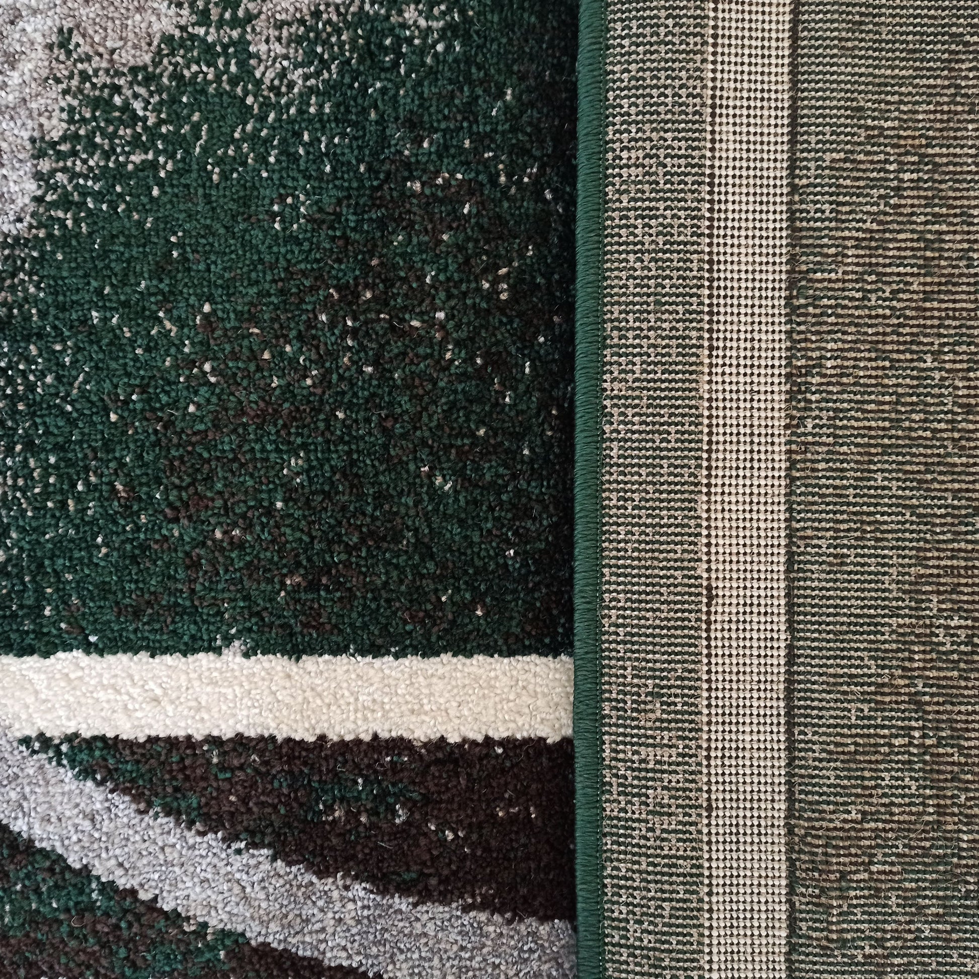 Tapis texturé à motifs abstraits vert foncé, blanc cassé, gris et brun, avec le revers tissé et le liseré vert visibles