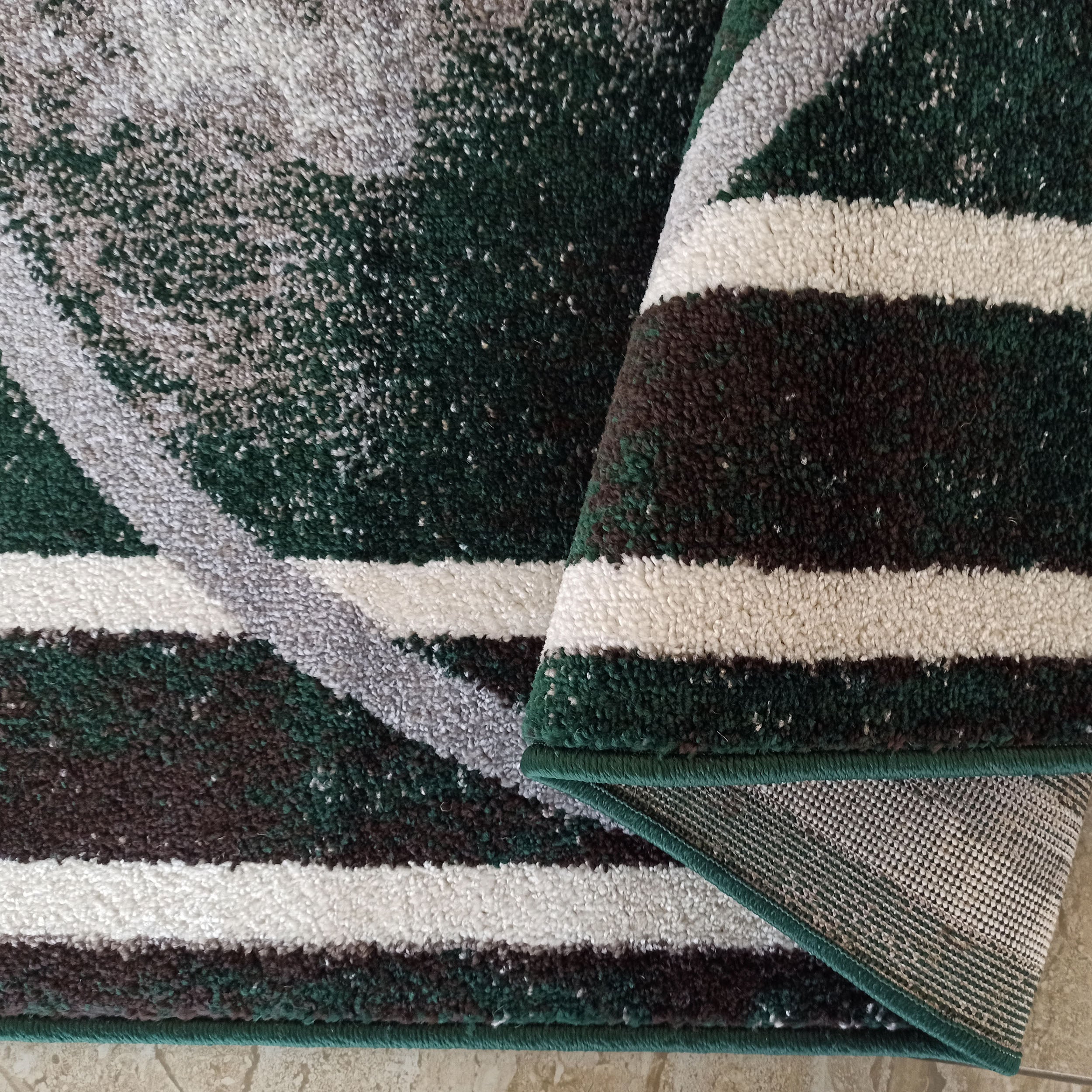 Tapis à poils longs aux motifs abstraits et bandes vert foncé, gris, marron et blanc, dont une partie est enroulée