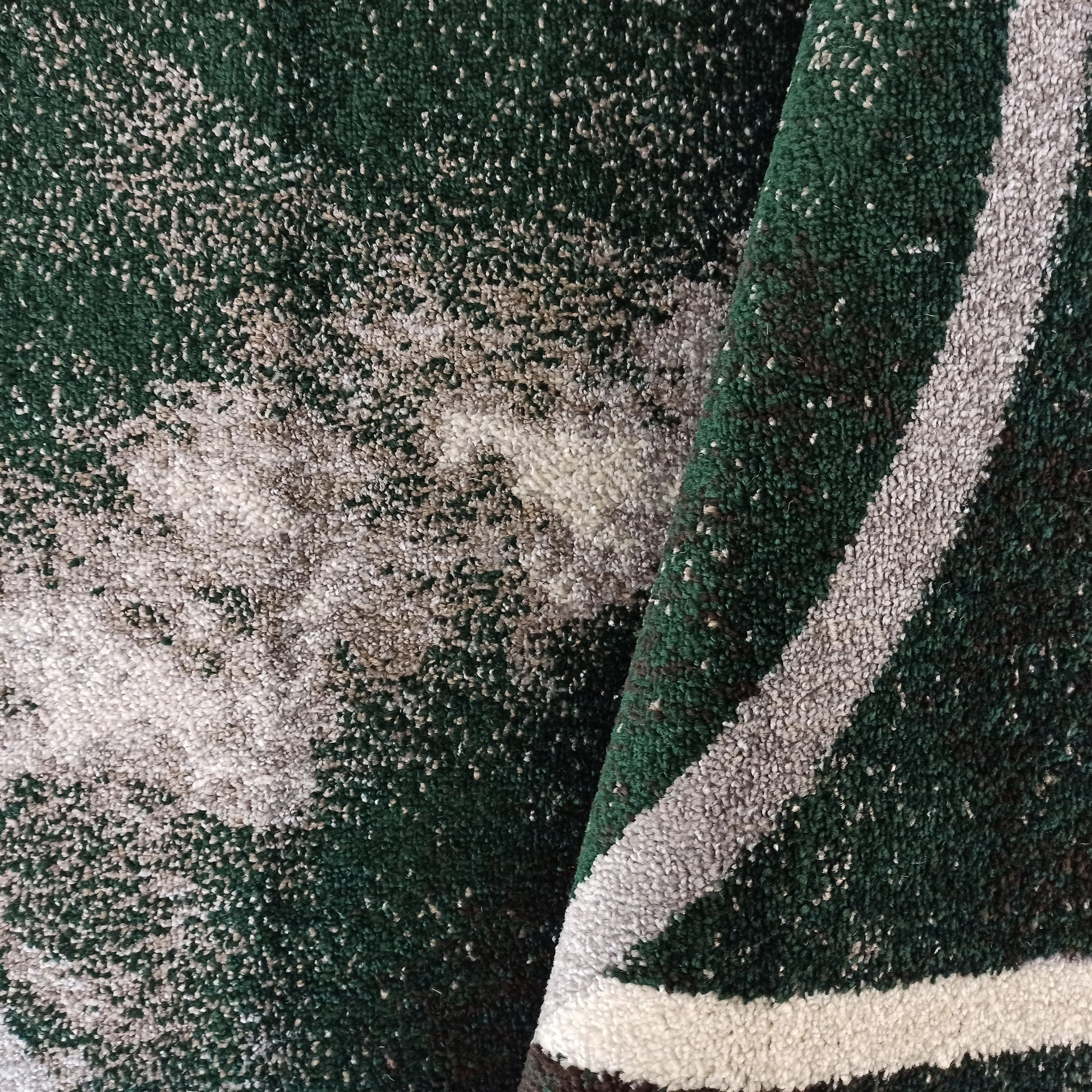 Tapis vert foncé à la texture dense et mouchetée de blanc et beige, avec des bandes grises et blanches sur le pli