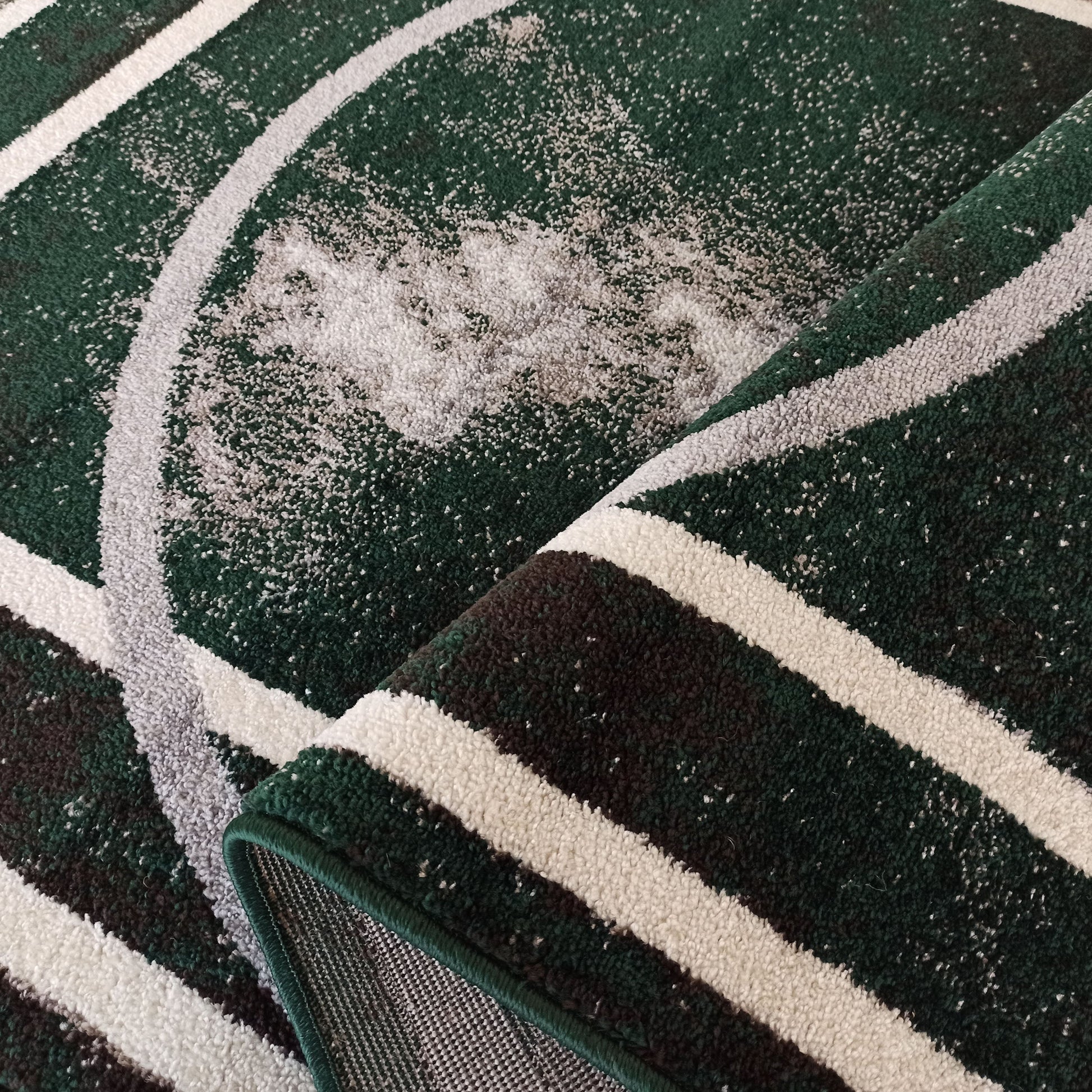 Tapis à motifs de bandes courbes vertes, blanches et grises. Sa surface est texturée et le tapis est partiellement roulé, montrant son envers