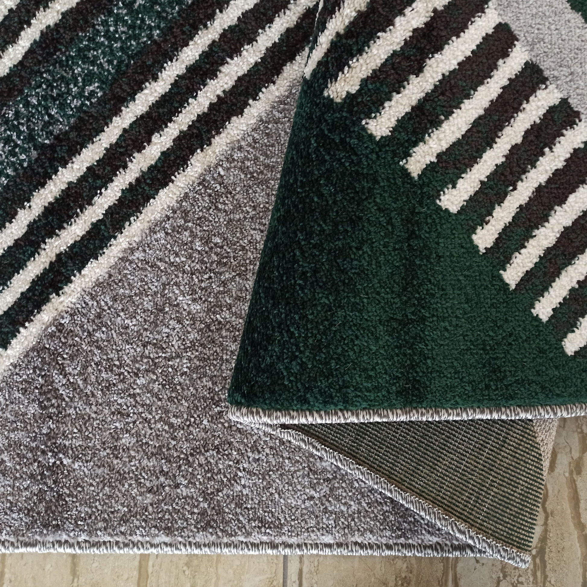 Tapis shaggy à motif géométrique de rayures diagonales vertes, marron et blanches, révélant son envers gris chiné