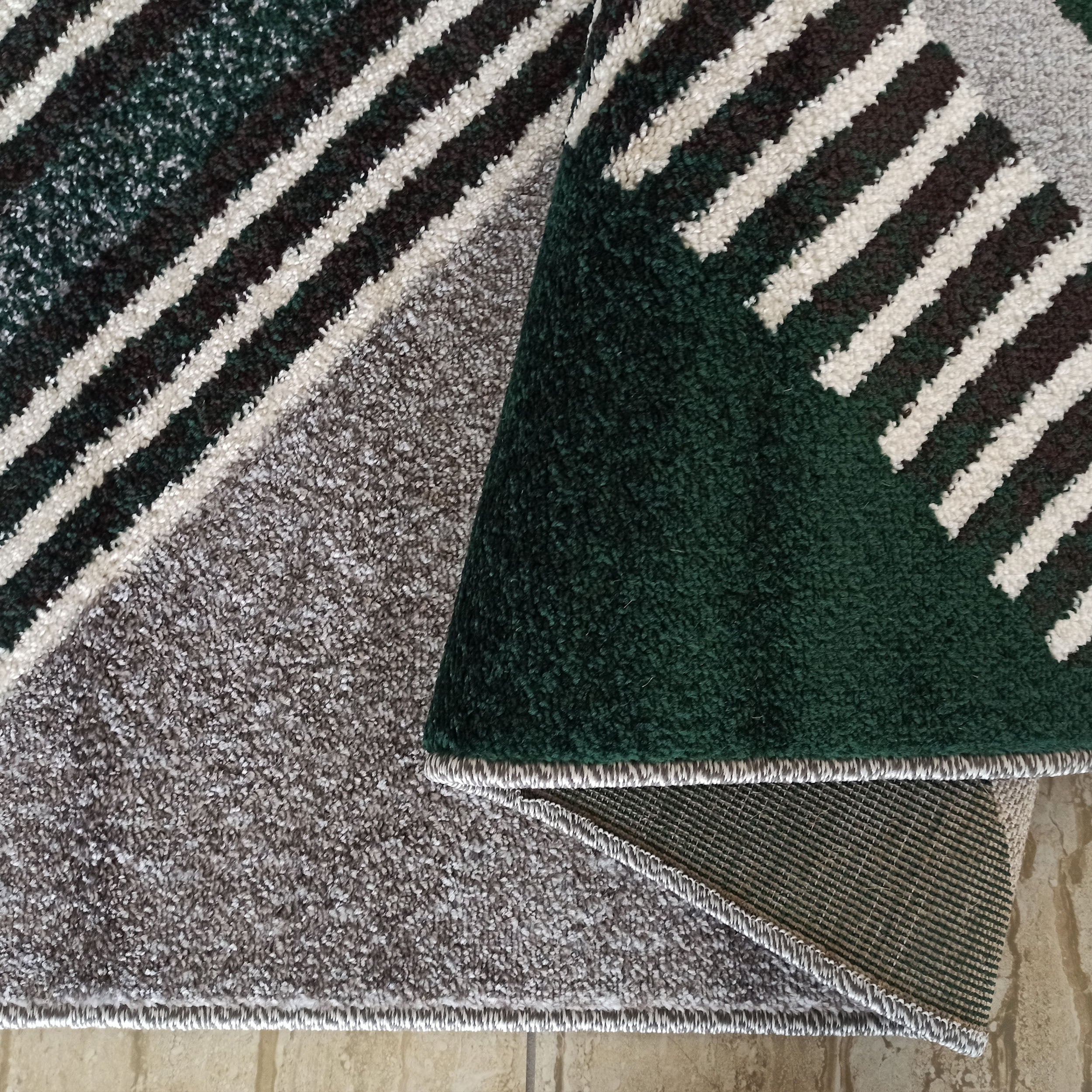 Tapis shaggy à motif géométrique de rayures diagonales vertes, marron et blanches, révélant son envers gris chiné