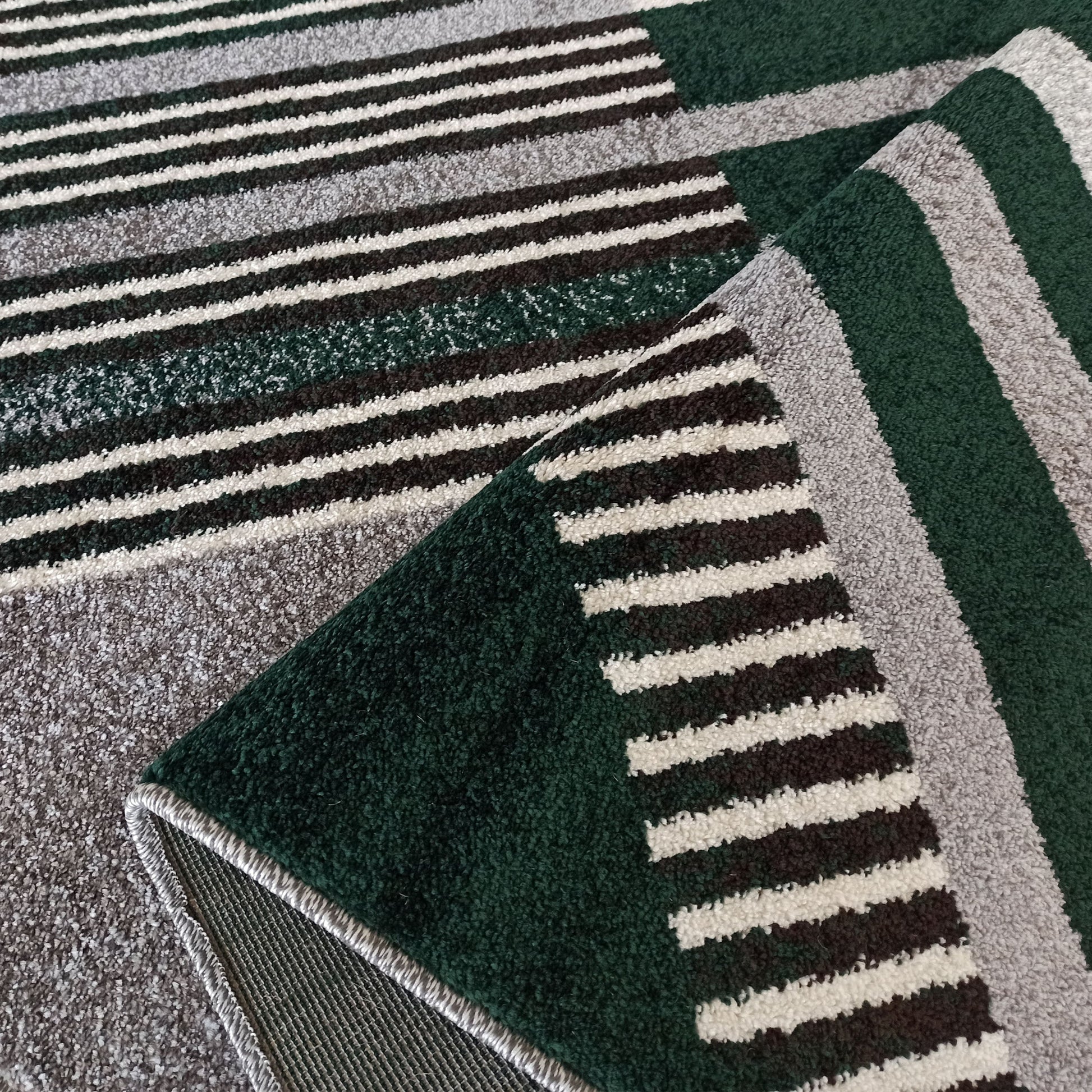 Tapis à poils longs avec des rayures larges vert foncé et gris chiné, alternant avec de fines rayures noires et blanches, plié