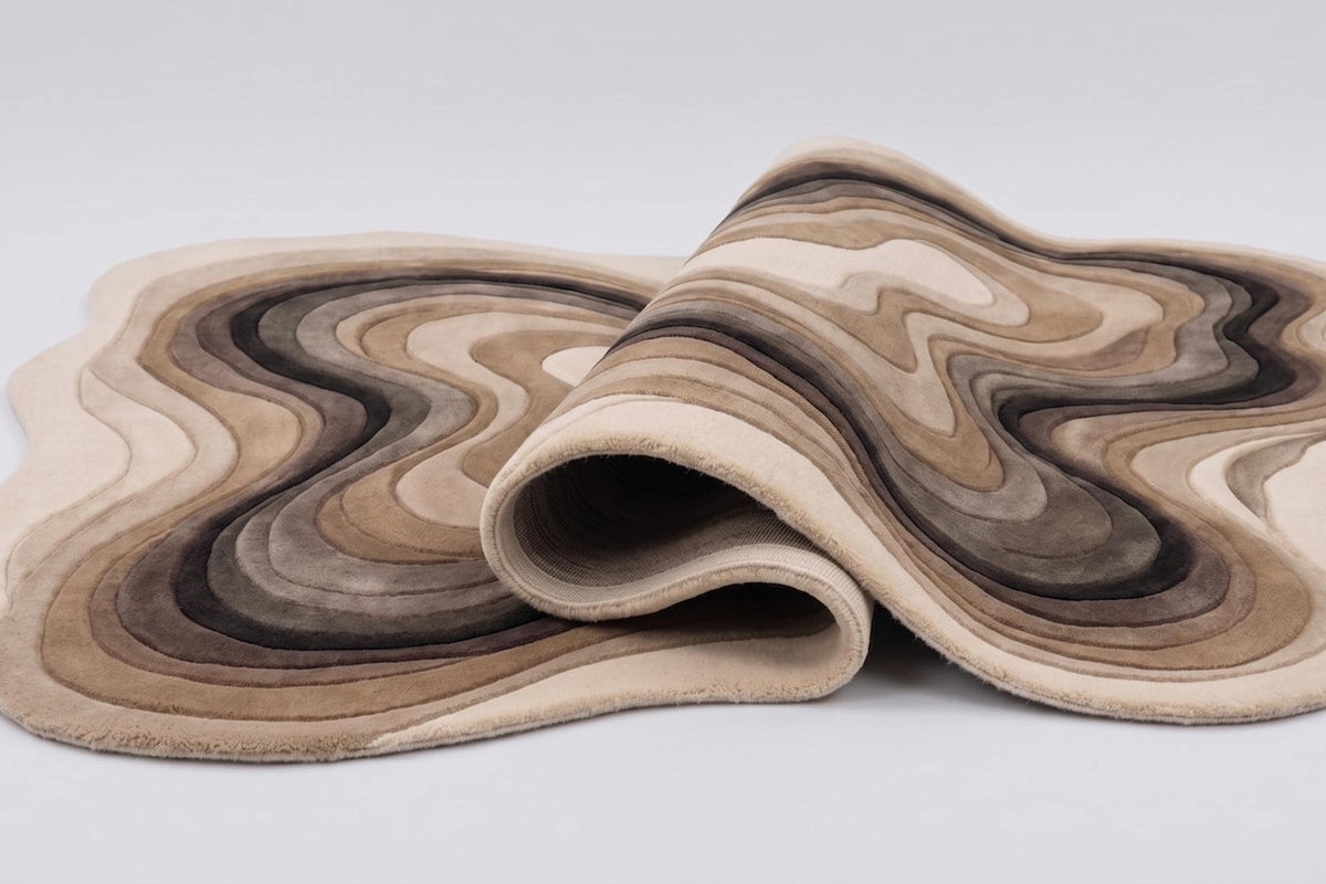 Tapis organique en laine aux strates beige, sable et brun, replié sur lui-même pour montrer sa souplesse et son relief