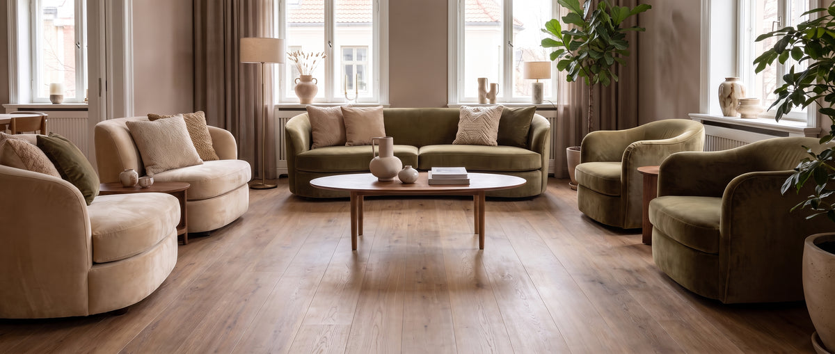 Pièce de vie lumineuse au parquet clair et sol nu, meublée d'un canapé vert olive et fauteuils de velours