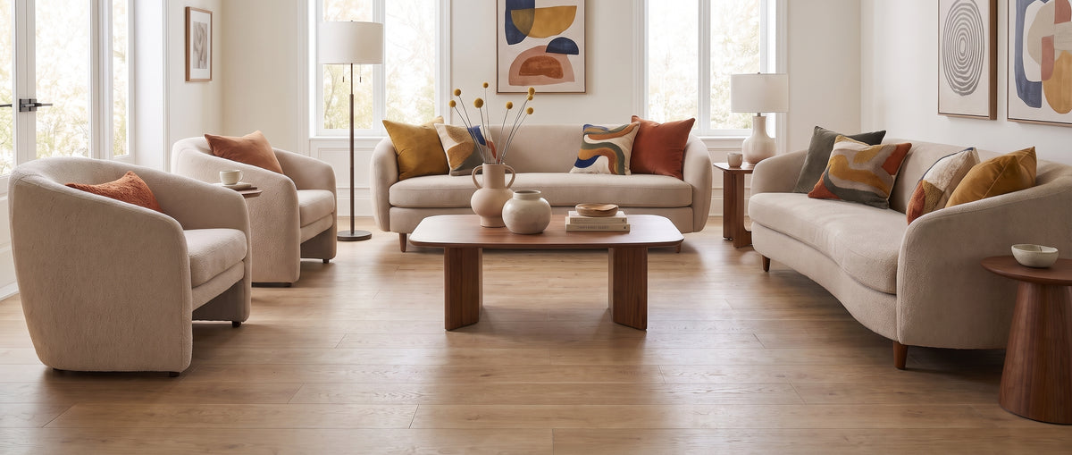 Salon lumineux sans tapis, au sol en bois clair, meublé de canapés et fauteuils crème aux coussins vifs et art mural