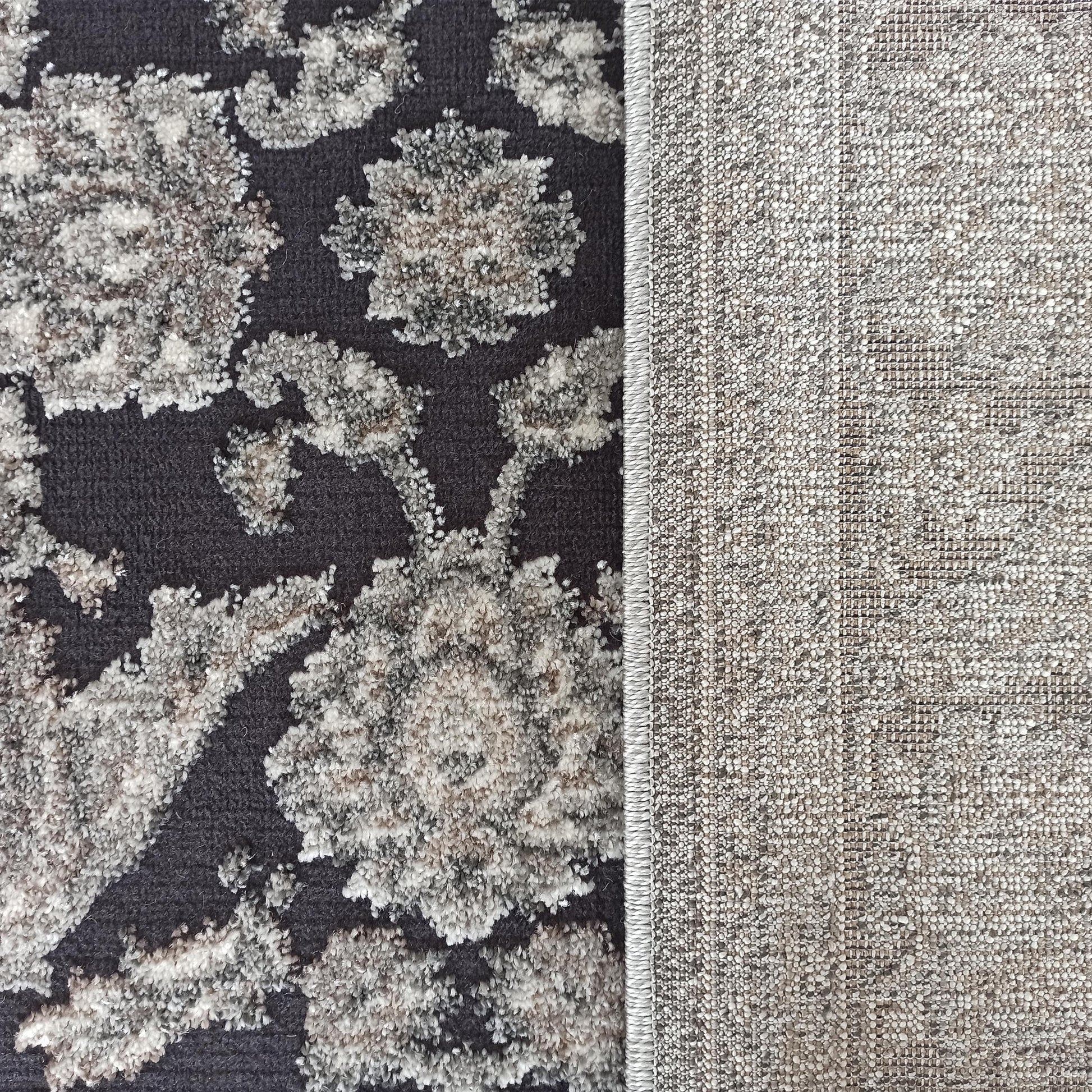 Tapis gris foncé avec des motifs floraux texturés gris clair et beige, et l'envers tissé en toile beige-gris