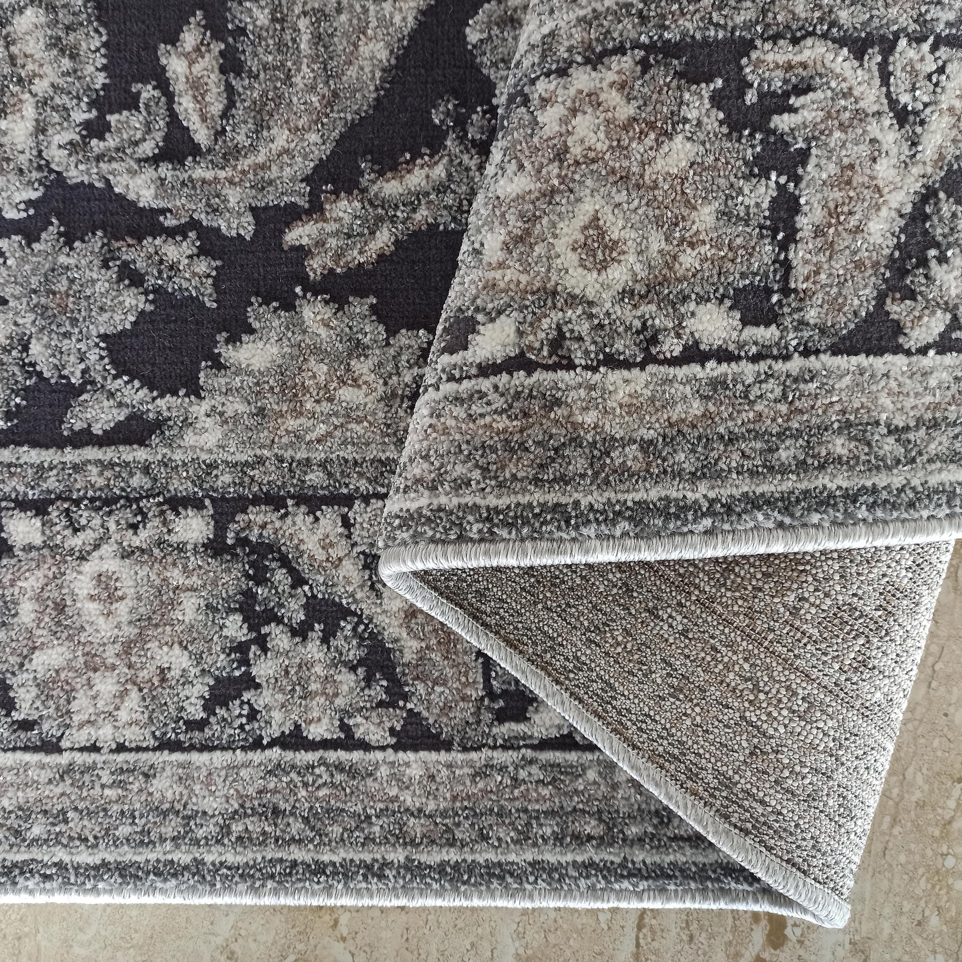 Tapis gris anthracite à motifs ornementaux clairs, avec une bordure cousue et le revers tissé apparent