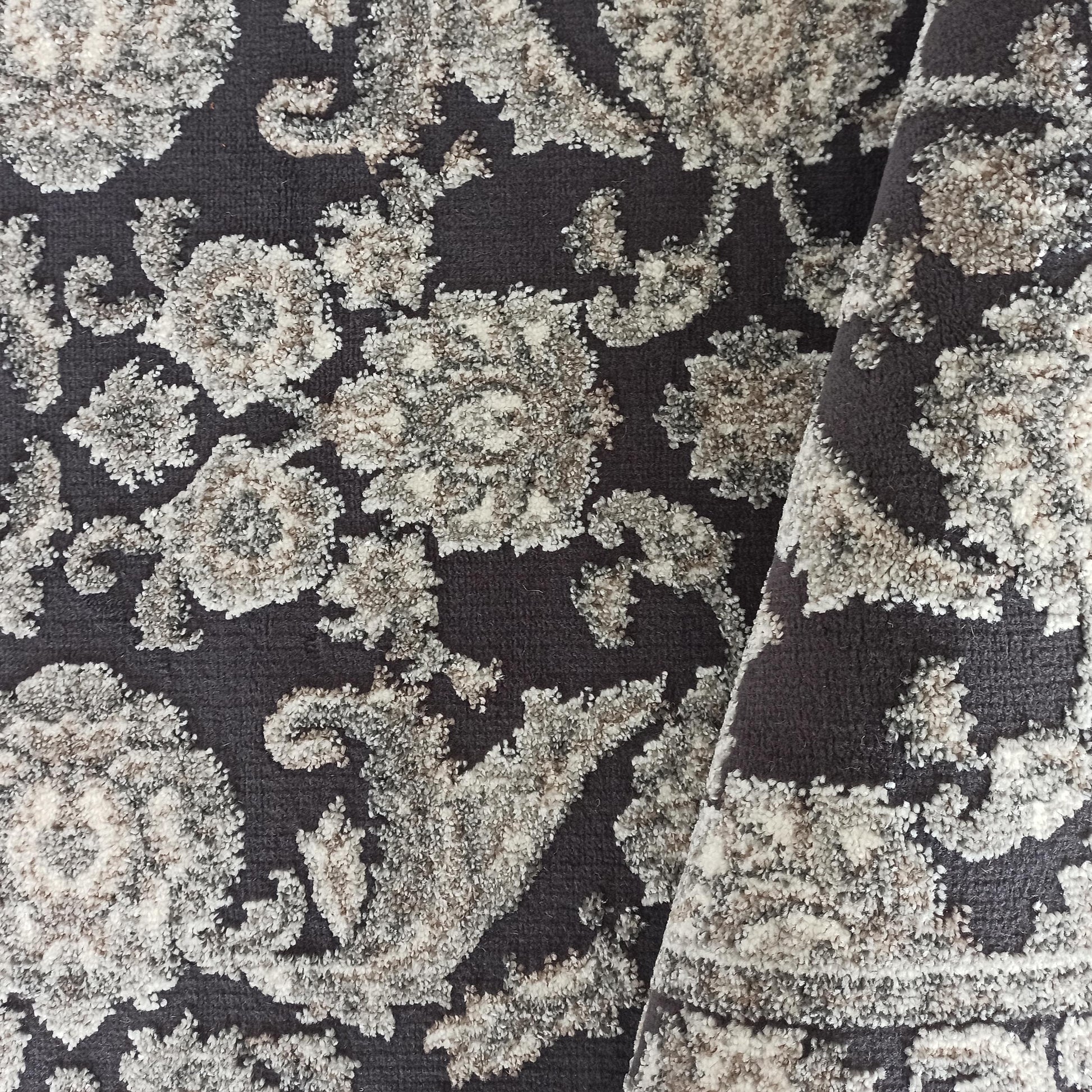 Tapis gris anthracite à motifs floraux et ornementaux clairs, avec une texture bouclée en relief mêlant crème, gris clair et marron
