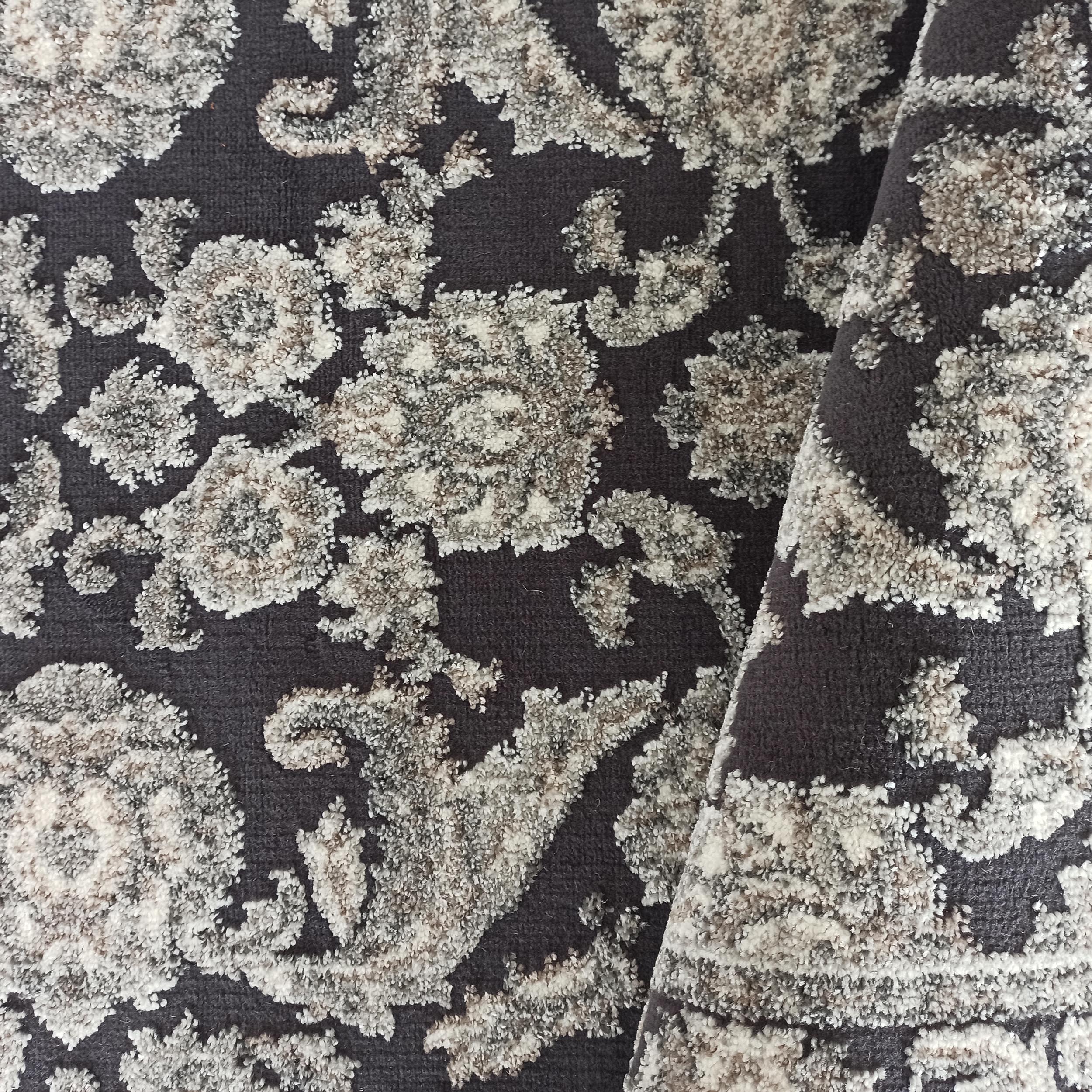 Tapis gris anthracite à motifs floraux et ornementaux clairs, avec une texture bouclée en relief mêlant crème, gris clair et marron