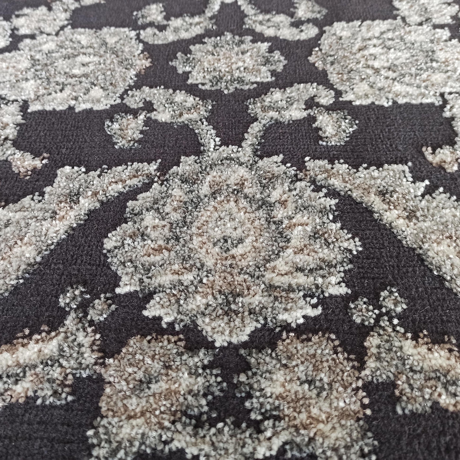 Tapis gris foncé avec des motifs floraux en relief de textures variées, aux tons de gris clair, blanc et beige