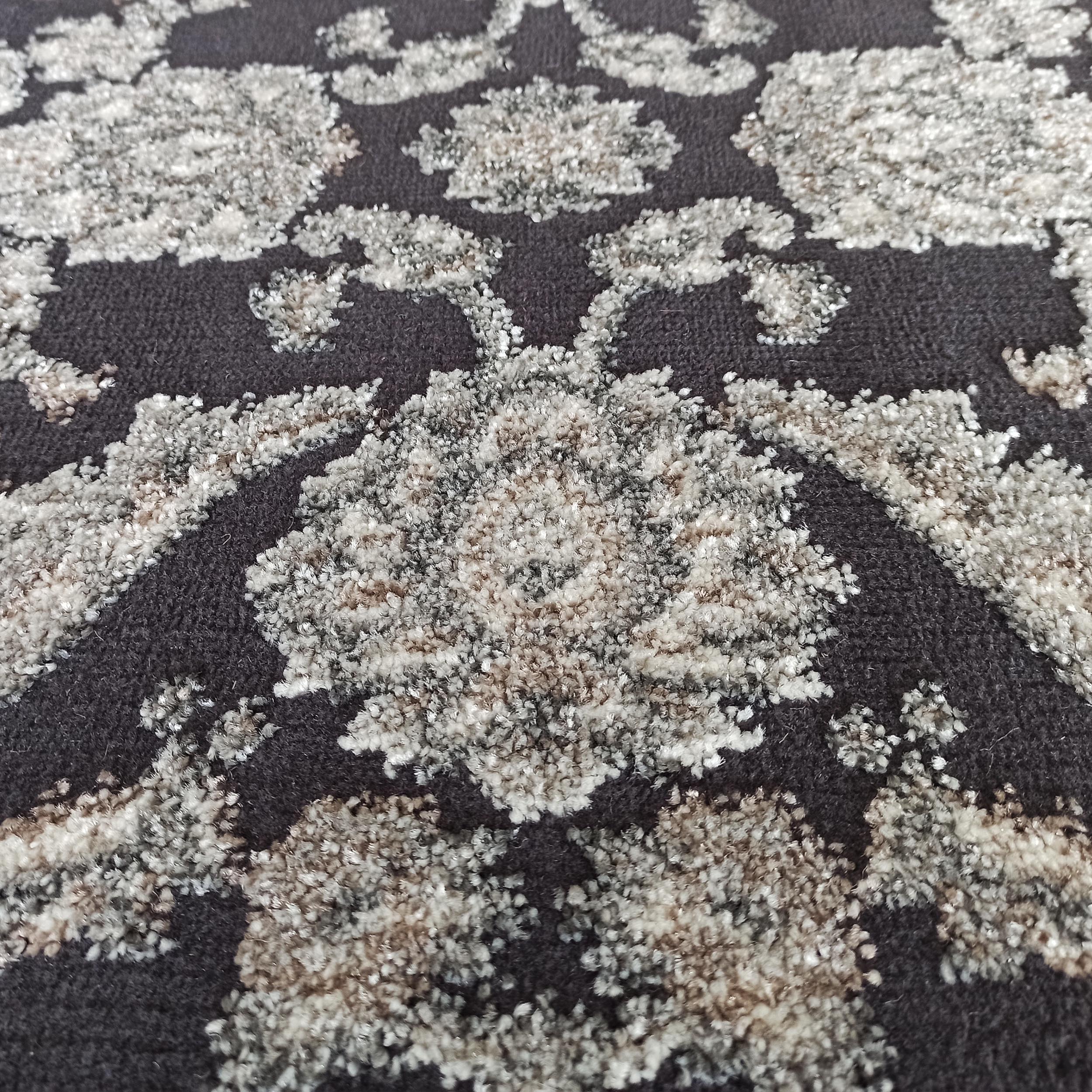 Tapis gris foncé avec des motifs floraux en relief de textures variées, aux tons de gris clair, blanc et beige