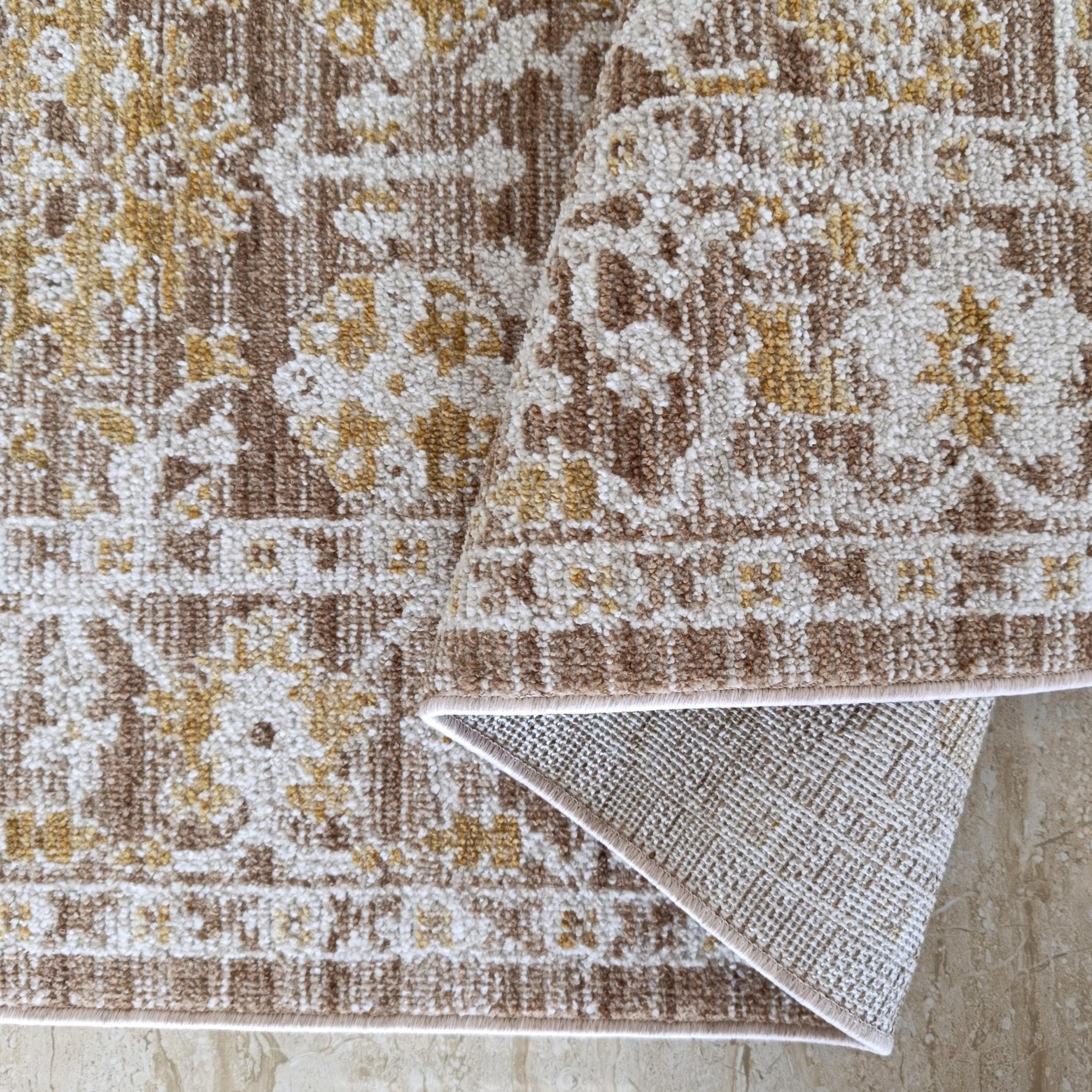 Tapis texturé crème, marron clair, or à motifs ornementaux, roulé sur carrelage beige marbré, envers tissé apparent