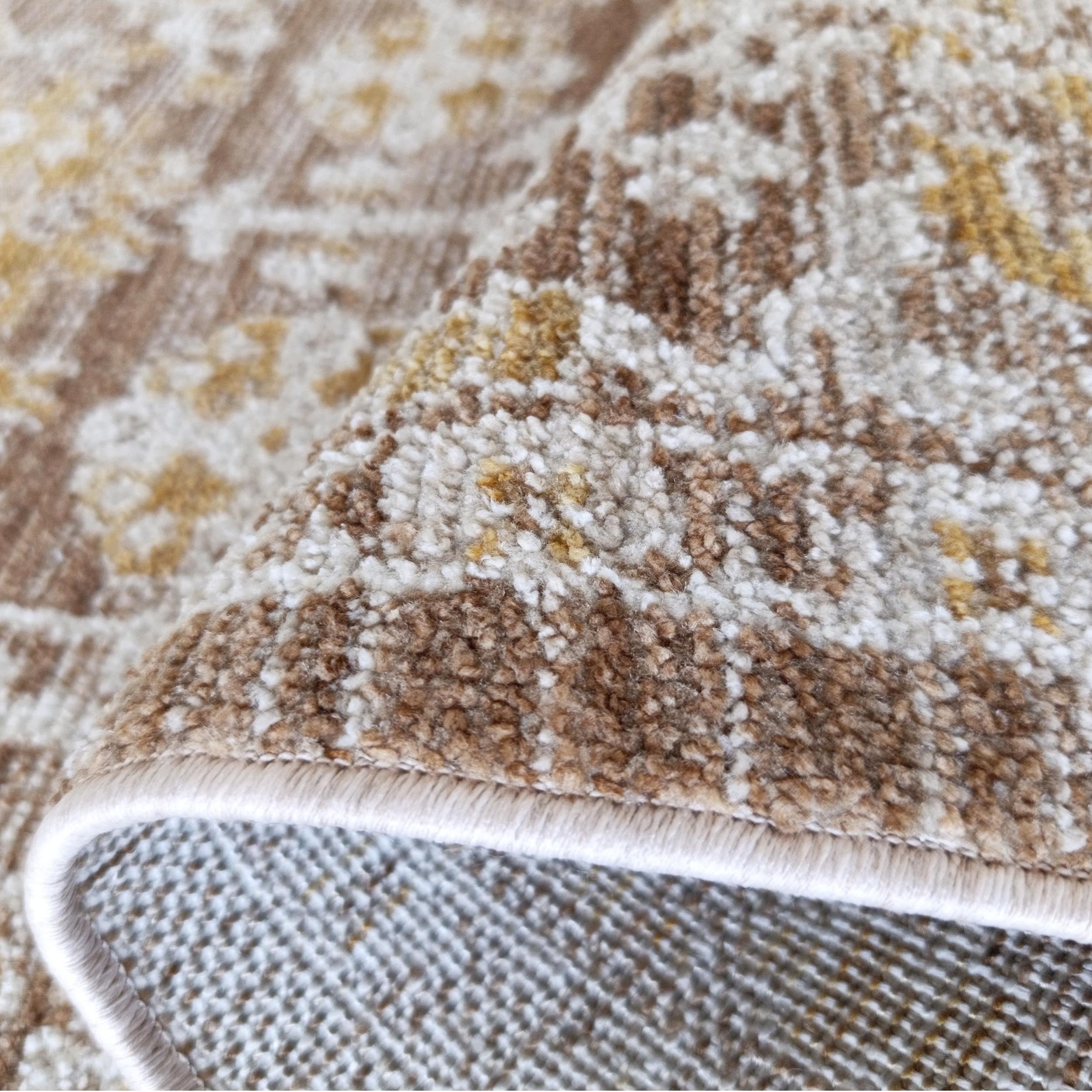 Tapis beige clair à motifs ornementaux marron et jaunes, à la texture moelleuse et au revers tissé, partiellement roulé