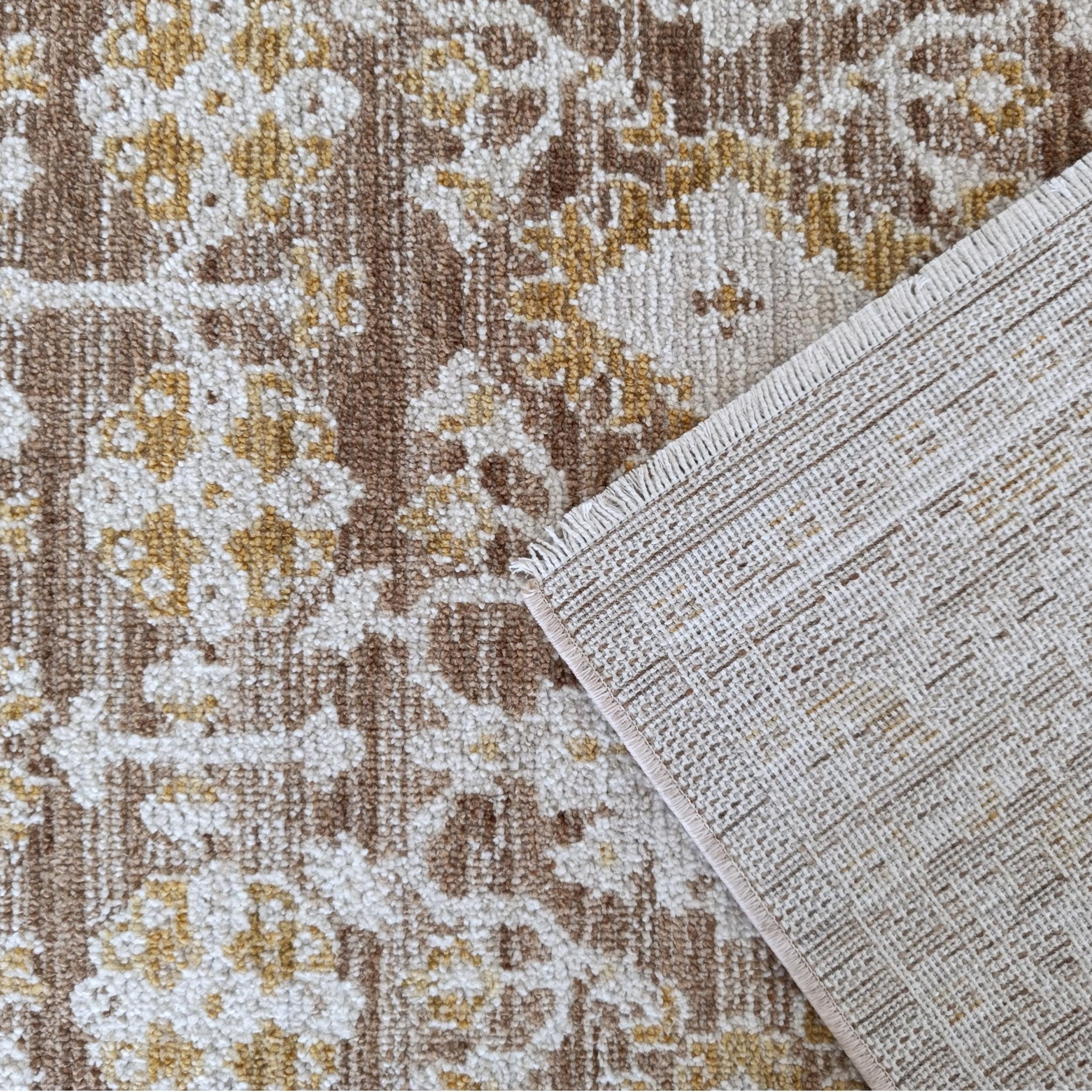 Tapis moelleux floral marron, beige et jaune dont un coin, plié, révèle son envers et sa bordure frangée