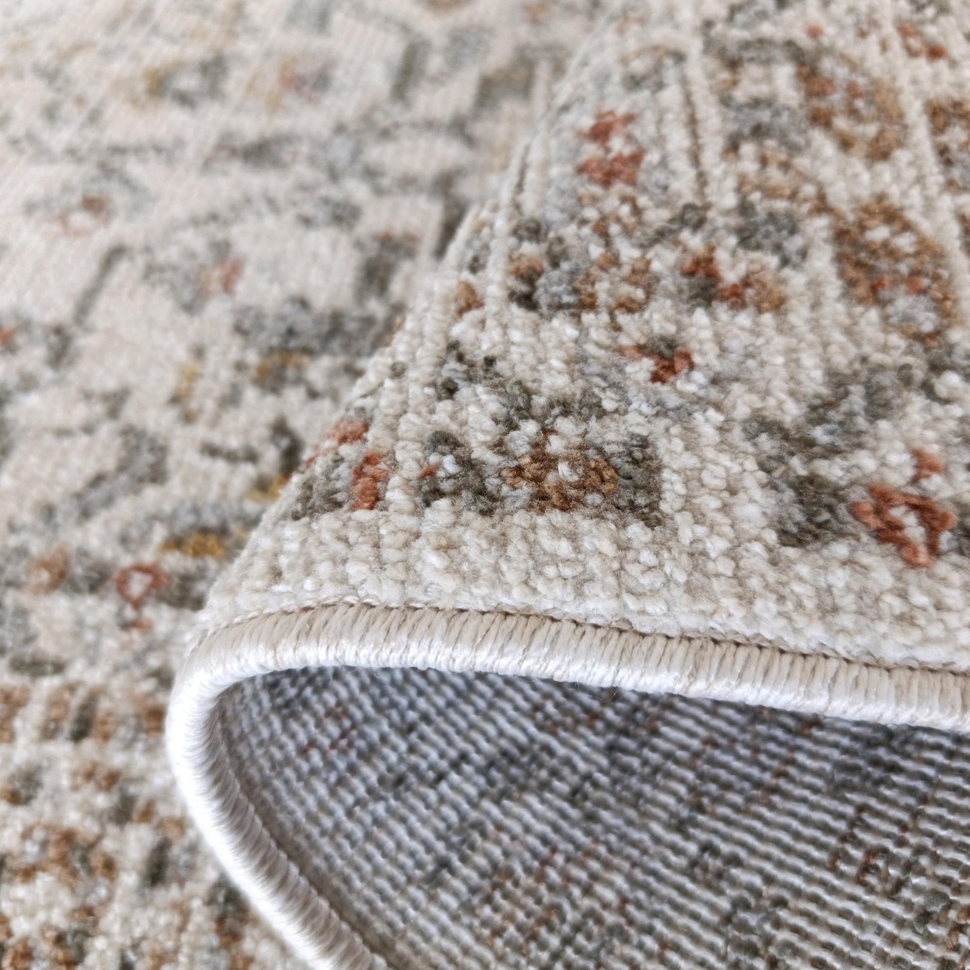 Un tapis roulé aux motifs crème, marron, gris et orangés, montre sa surface texturée et son envers tissé avec sa bordure