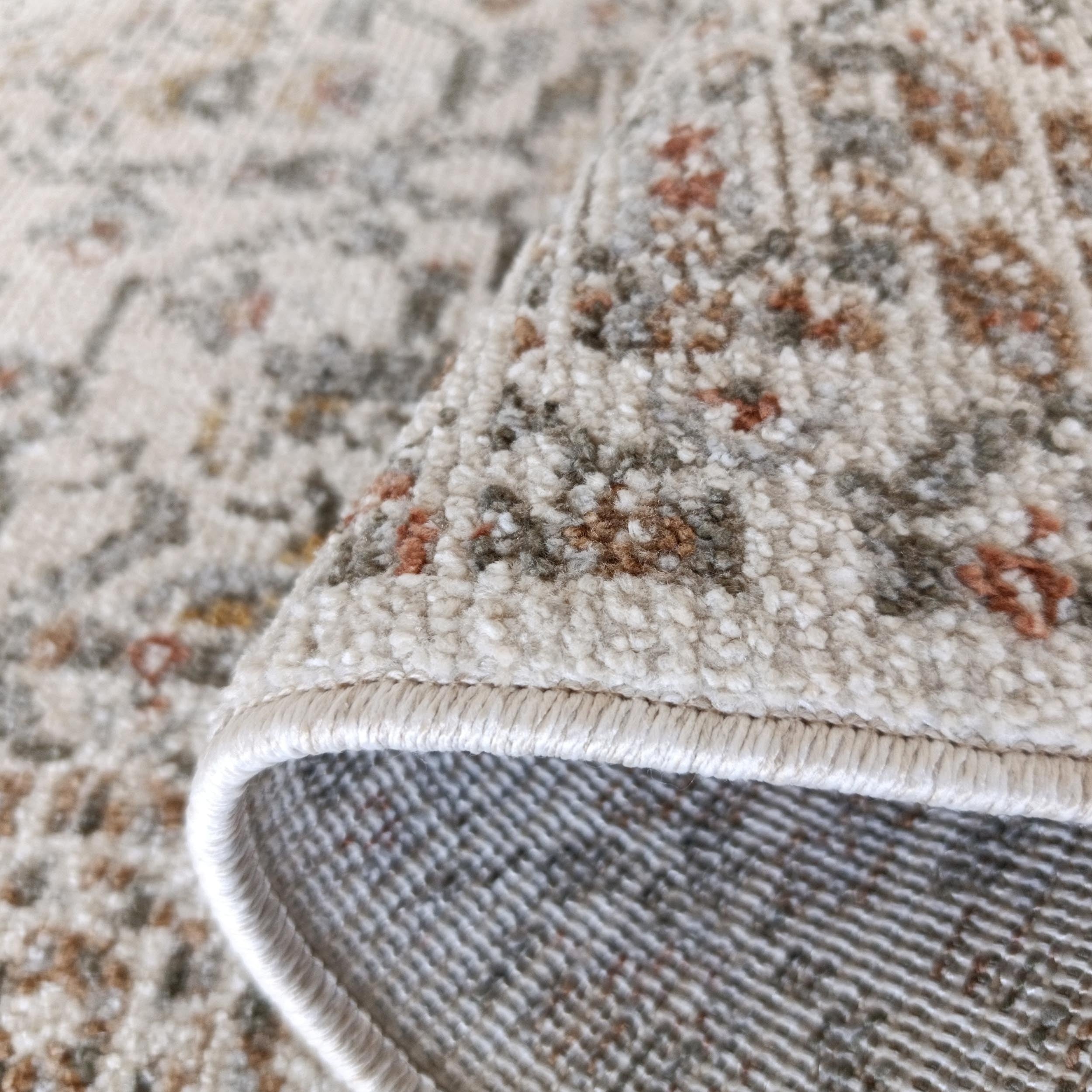 Un tapis roulé aux motifs crème, marron, gris et orangés, montre sa surface texturée et son envers tissé avec sa bordure