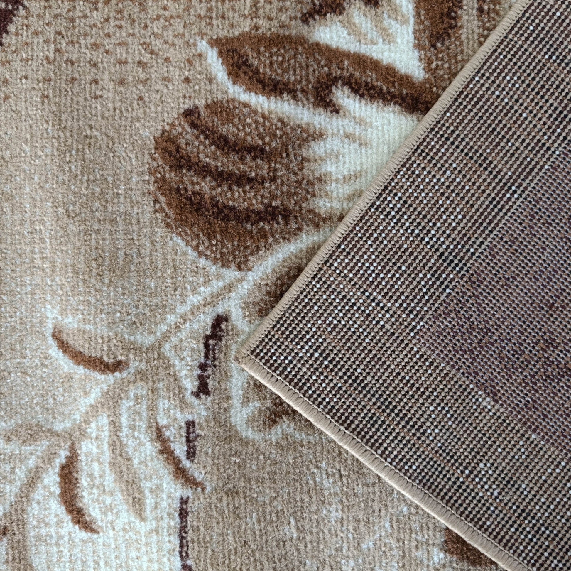 Tapis beige à motifs floraux marron, un coin relevé dévoile l'envers tissé de points beiges et bruns, et sa bordure cousue