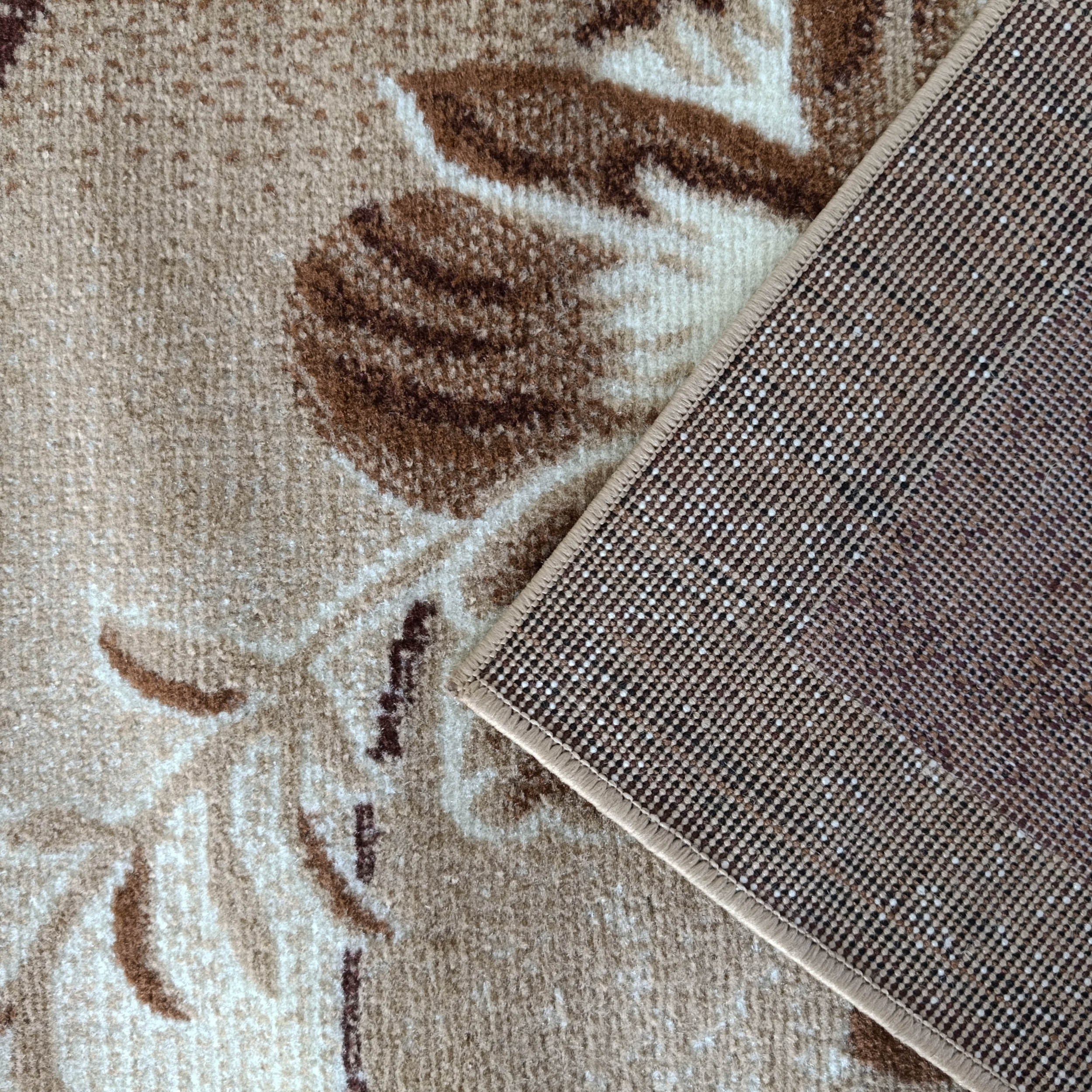 Tapis beige à motifs floraux marron, un coin relevé dévoile l'envers tissé de points beiges et bruns, et sa bordure cousue
