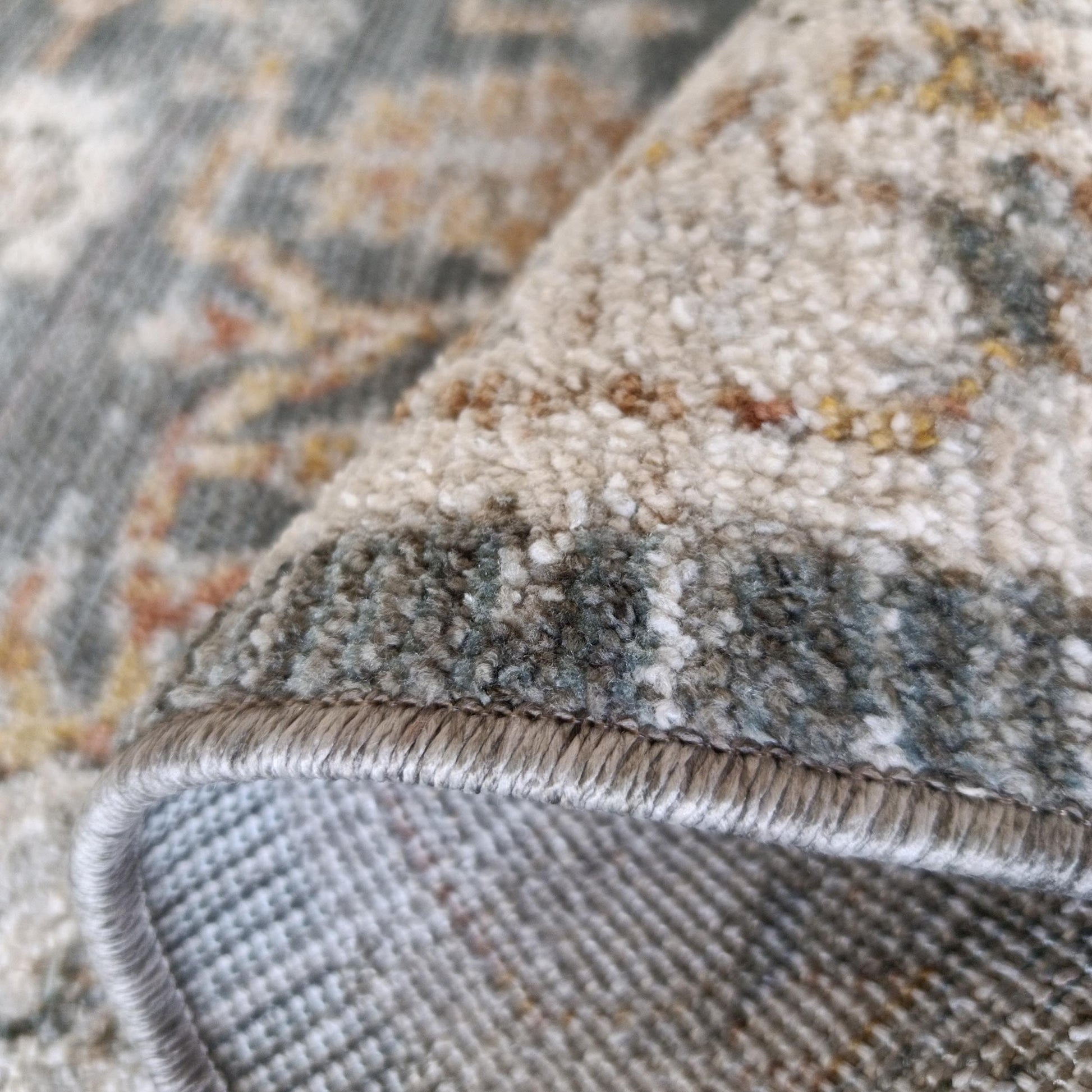 Tapis aux motifs complexes beige, gris-vert, rouille et jaune, roulé montrant texture duveteuse et dessous tissé