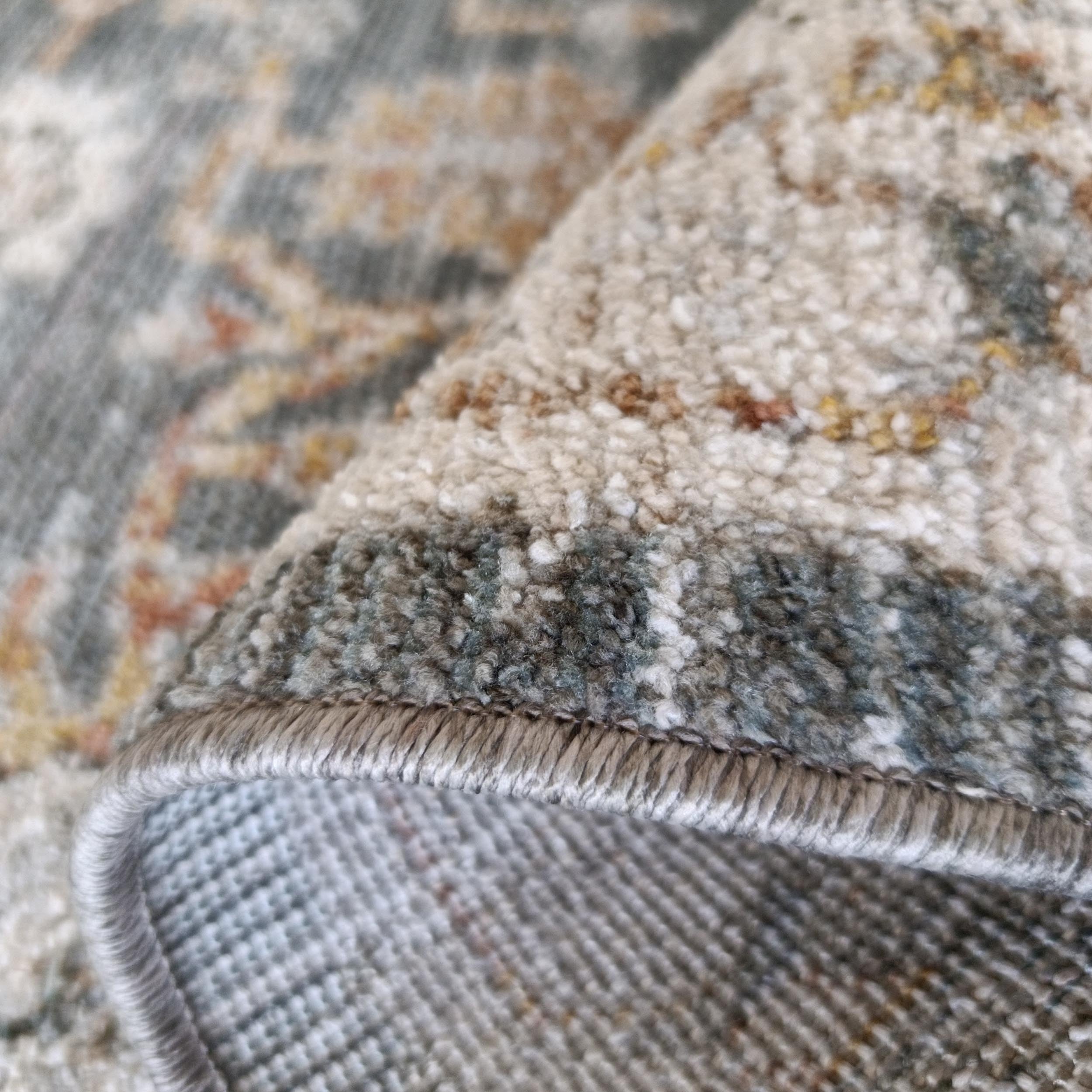 Tapis aux motifs complexes beige, gris-vert, rouille et jaune, roulé montrant texture duveteuse et dessous tissé