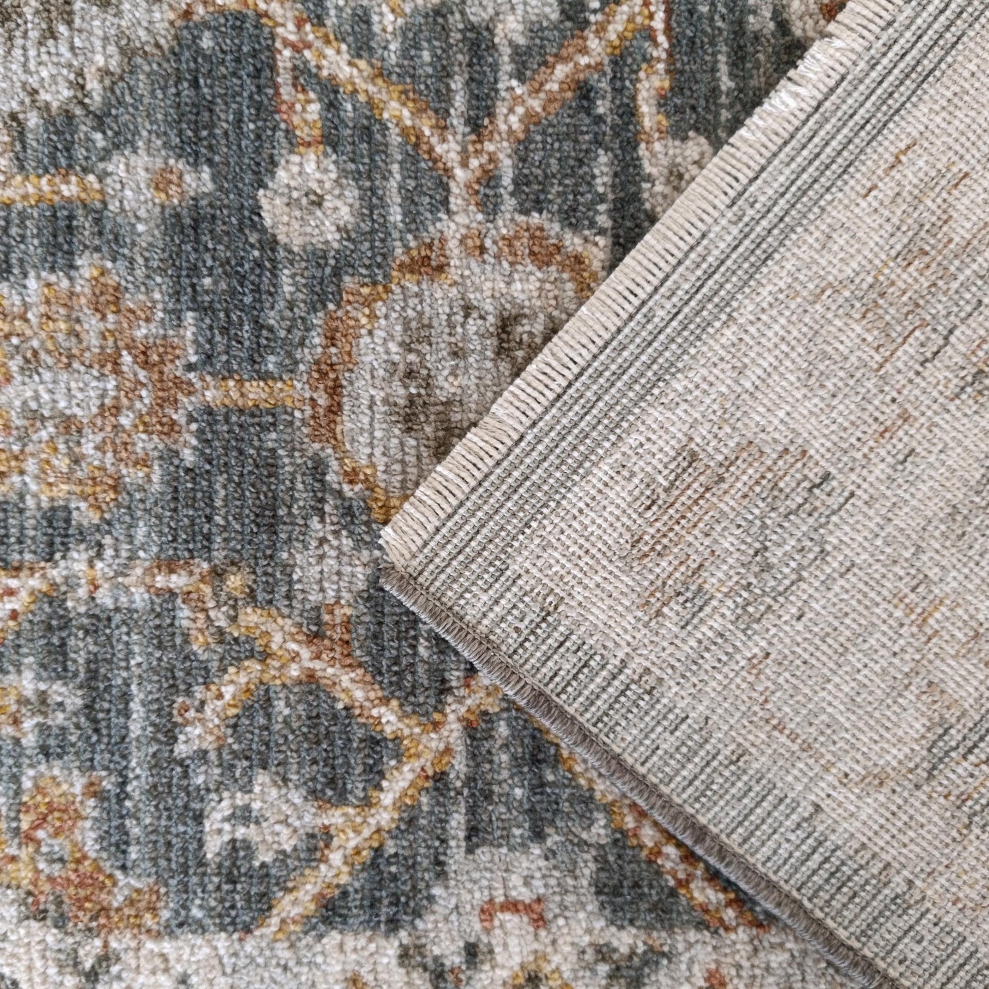 Tapis à poils courts gris-bleu à motifs ocre et rouille, le dos tissé clair replié laisse voir une bordure
