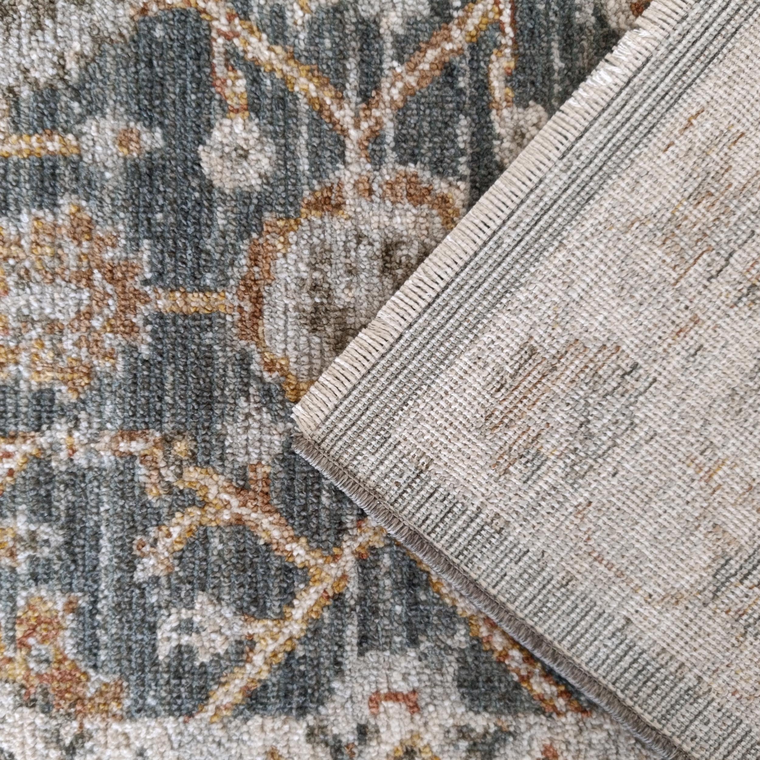 Tapis à poils courts gris-bleu à motifs ocre et rouille, le dos tissé clair replié laisse voir une bordure