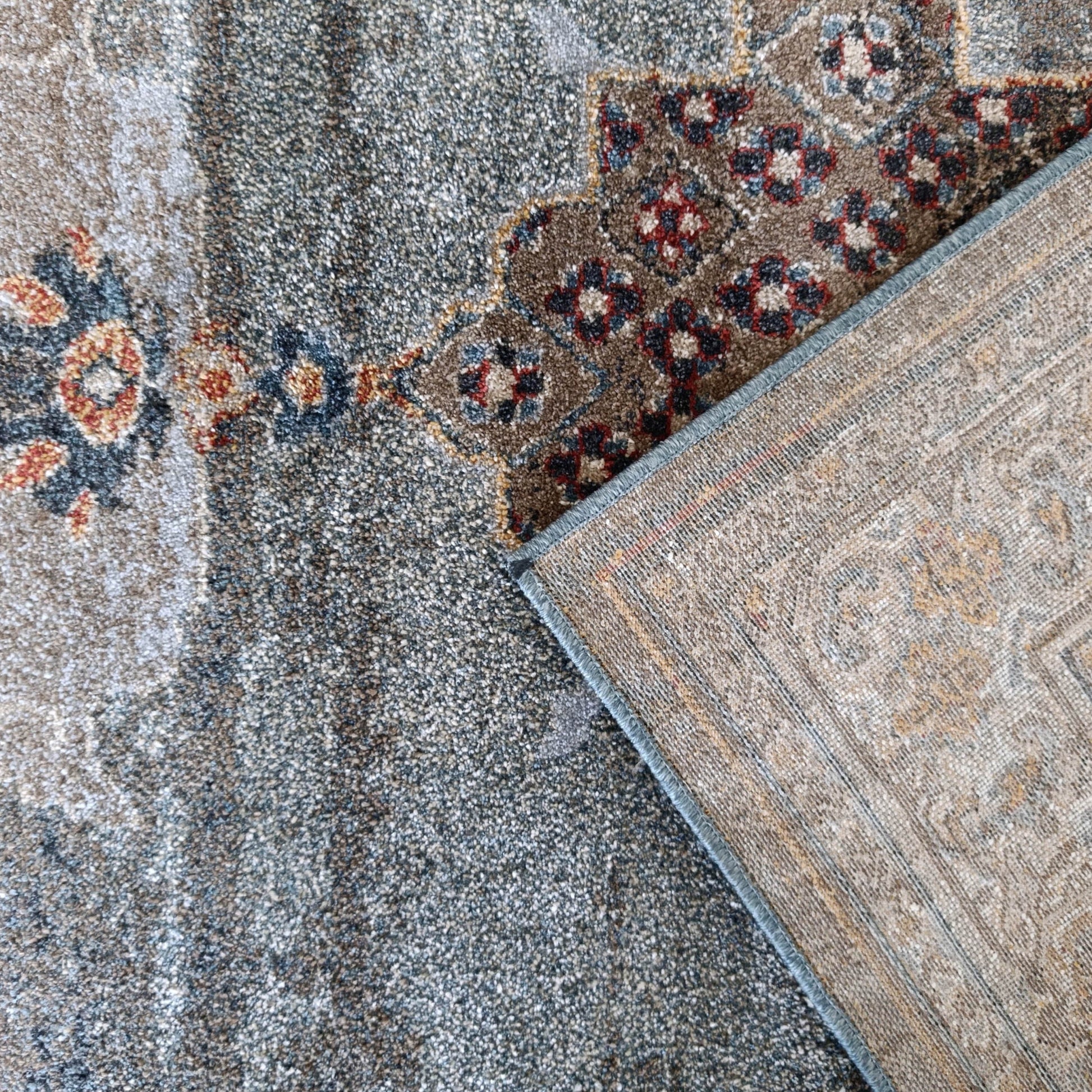 Tapis velu gris-bleu et marron à motifs floraux rouges et bleus, son envers tissé beige à bordure bleue