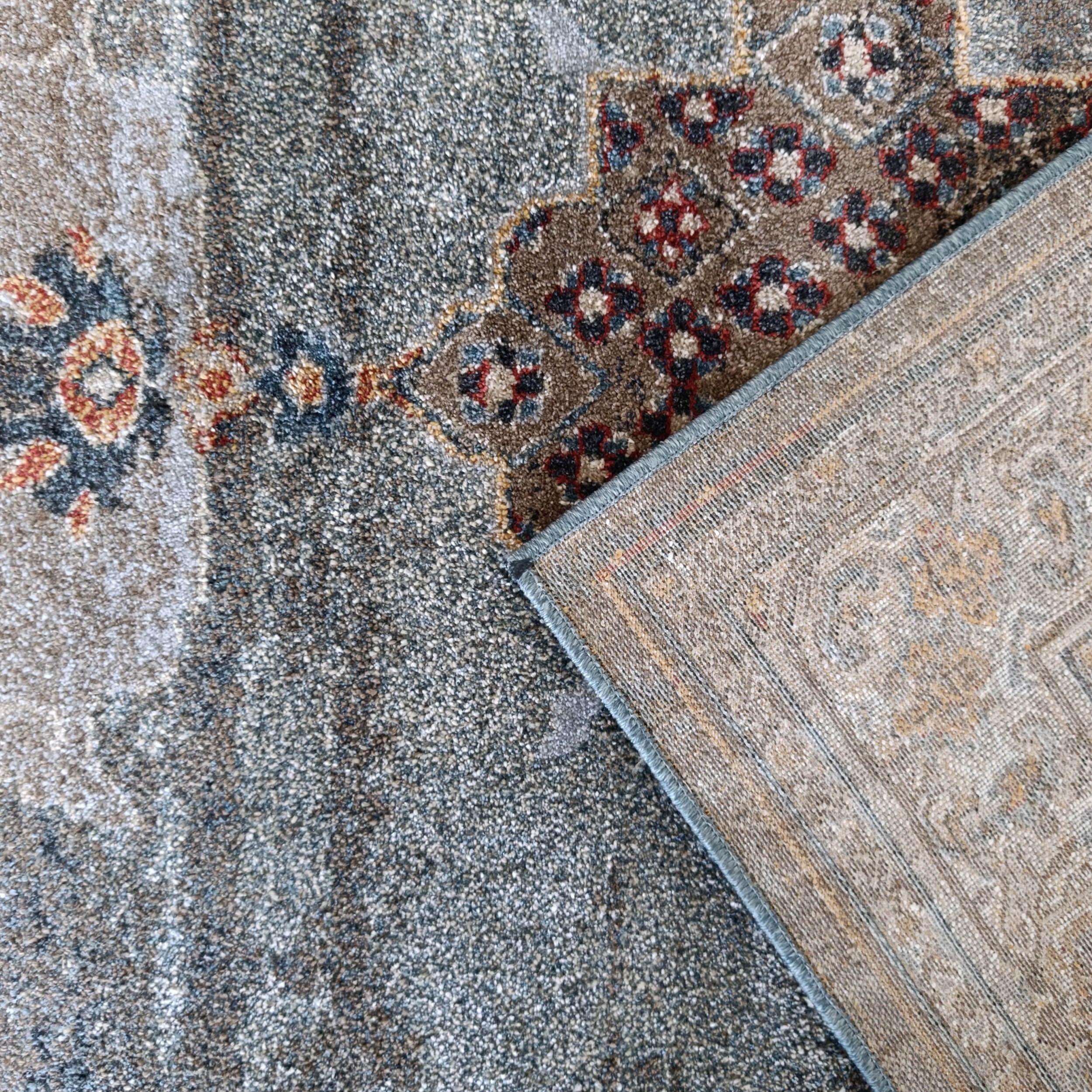 Tapis velu gris-bleu et marron à motifs floraux rouges et bleus, son envers tissé beige à bordure bleue