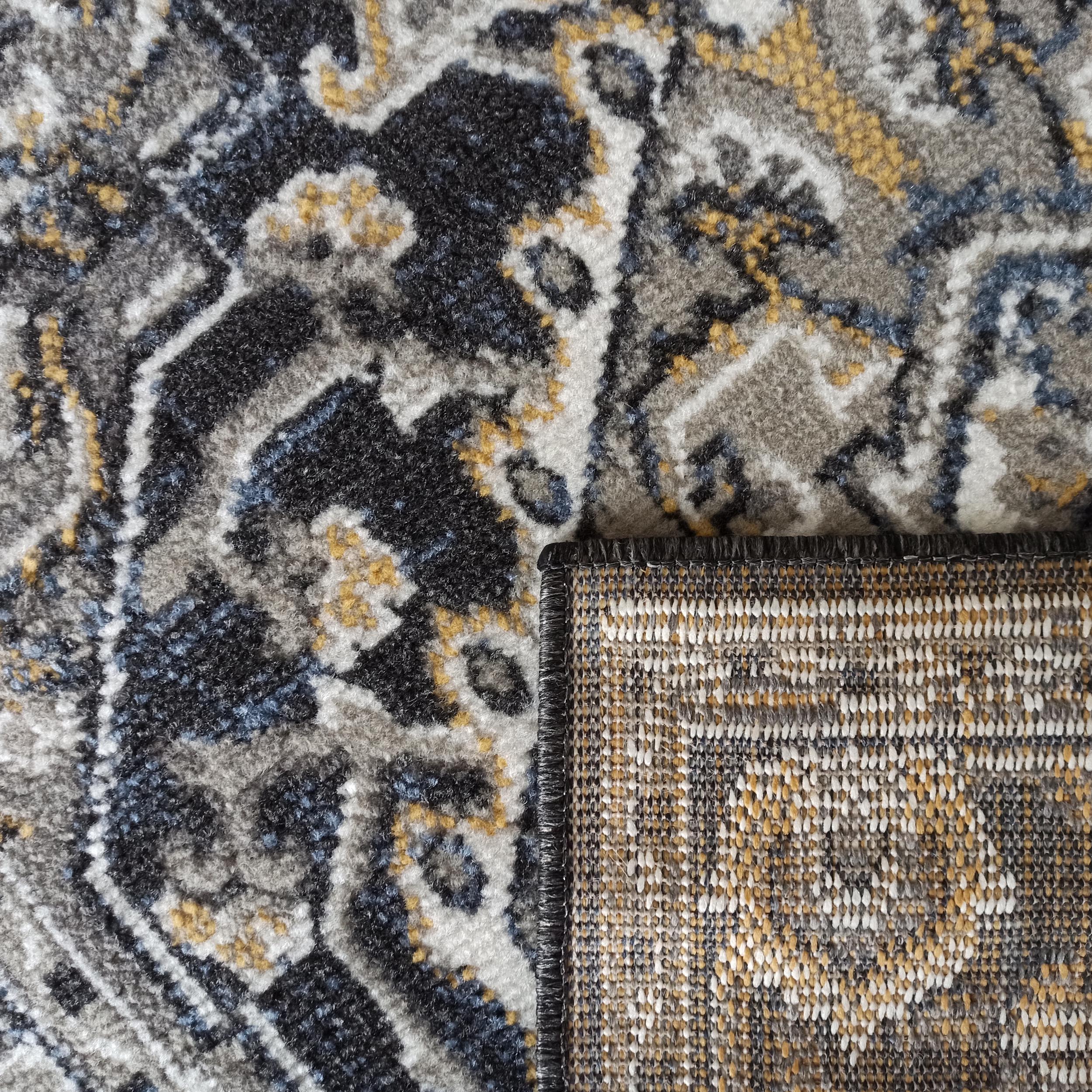 Tapis à poils longs avec un motif abstrait gris, noir, blanc, jaune et bleu, un coin plié révélant l'envers tissé