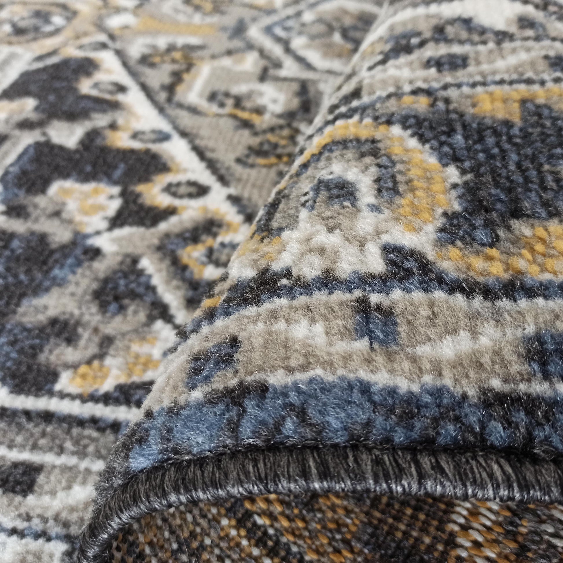 Gros plan sur un tapis roulé, texturé, aux motifs géométriques et ornementaux, en gris, bleu foncé, crème et jaune doré