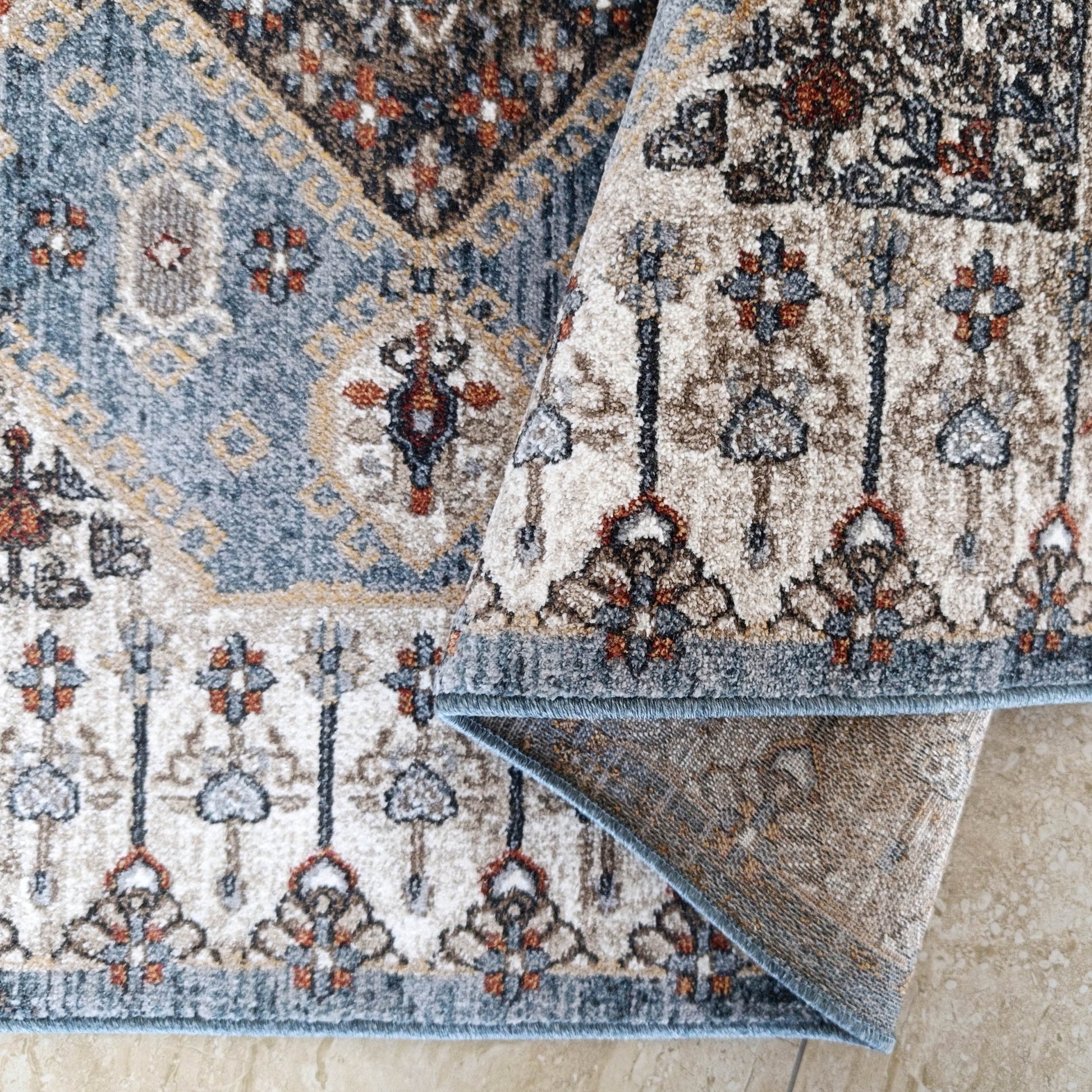 Tapis moelleux tissé à motifs complexes bleu gris, beige, marron et rouille sur un carrelage clair