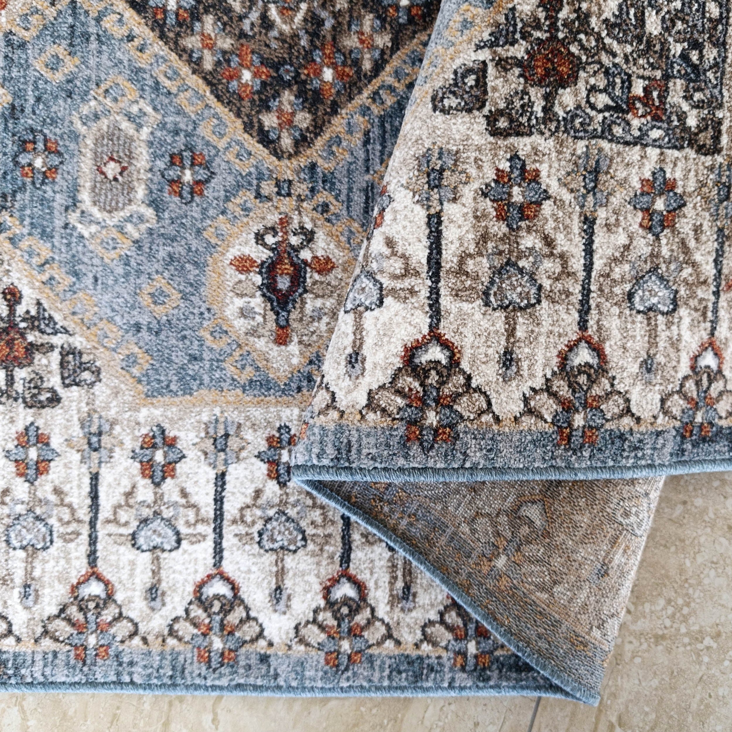 Tapis moelleux tissé à motifs complexes bleu gris, beige, marron et rouille sur un carrelage clair