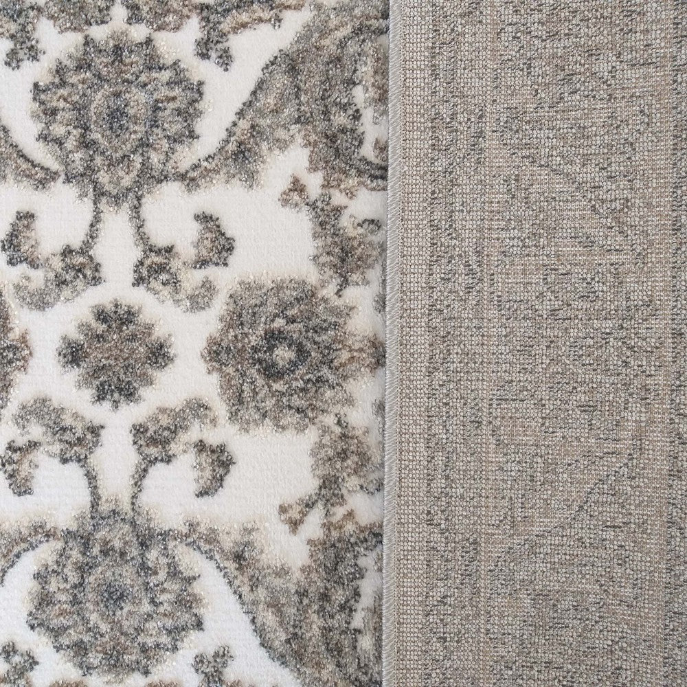 Tapis crème à motif ornemental gris et marron, sa texture moelleuse et son envers tissé beige sont visibles