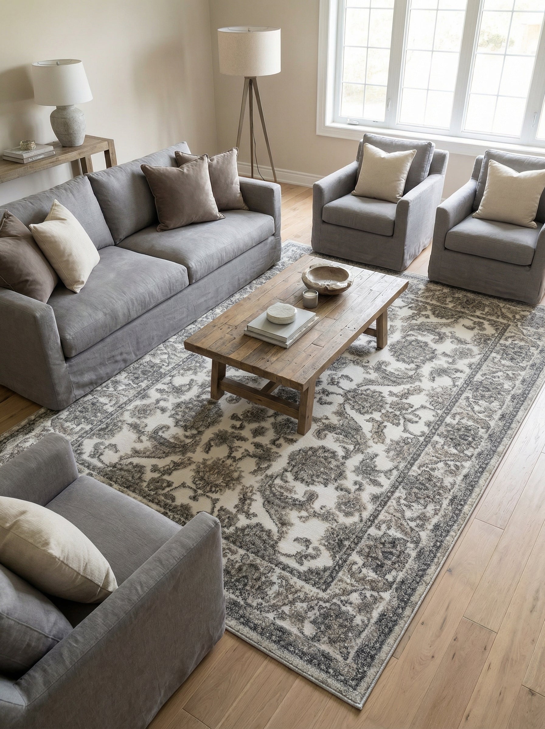Tapis rectangulaire crème et gris aux motifs floraux et ornementaux d'aspect vieilli, placé dans un salon clair