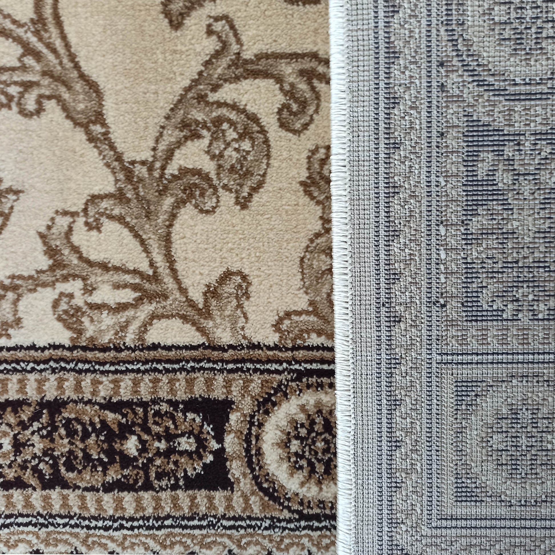 Tapis beige et marron à motifs floraux et bordure ornementale, partiellement roulé pour montrer son envers tissé grisâtre