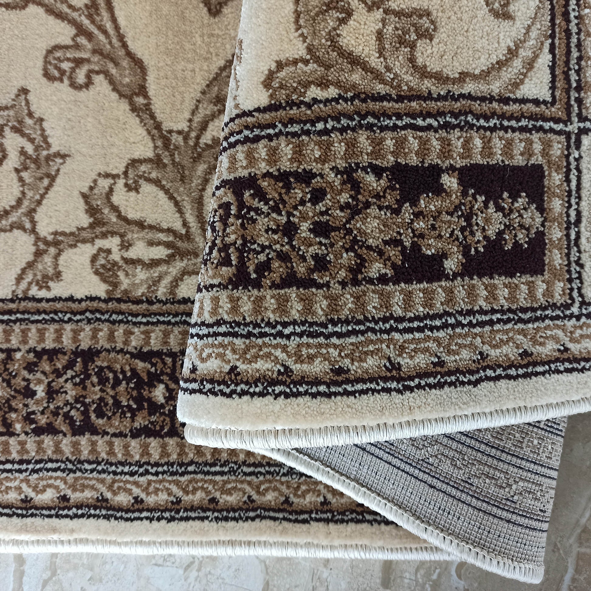 Tapis beige et marron avec des motifs floraux ornementaux, partiellement roulé, révélant sa texture et son envers