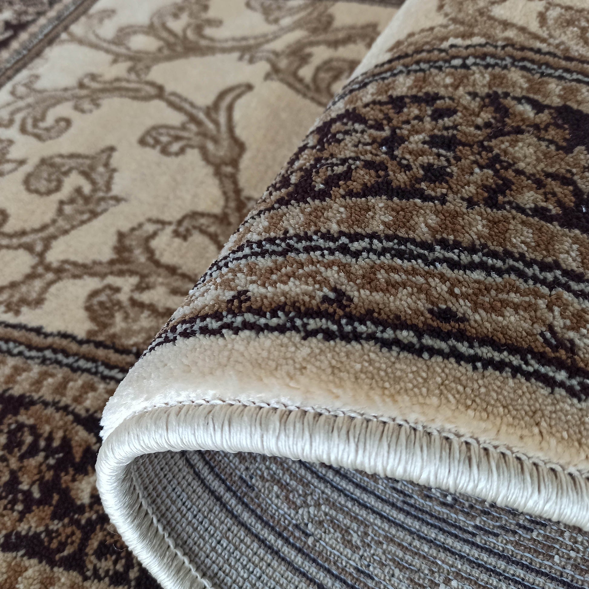 Tapis beige et marron enroulé, aux motifs floraux et rayés, laissant voir sa texture de poils et ses franges claires