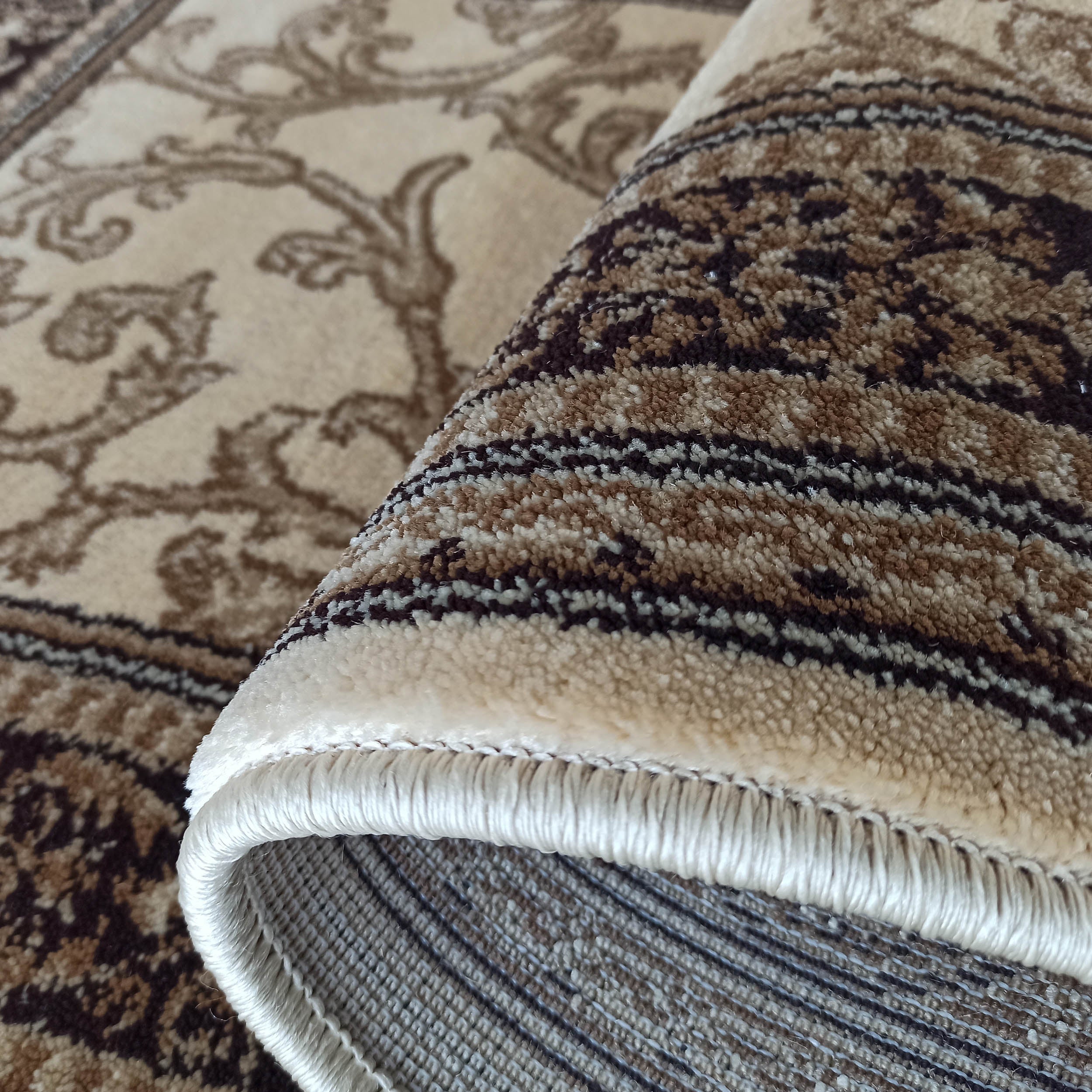 Tapis beige et marron enroulé, aux motifs floraux et rayés, laissant voir sa texture de poils et ses franges claires