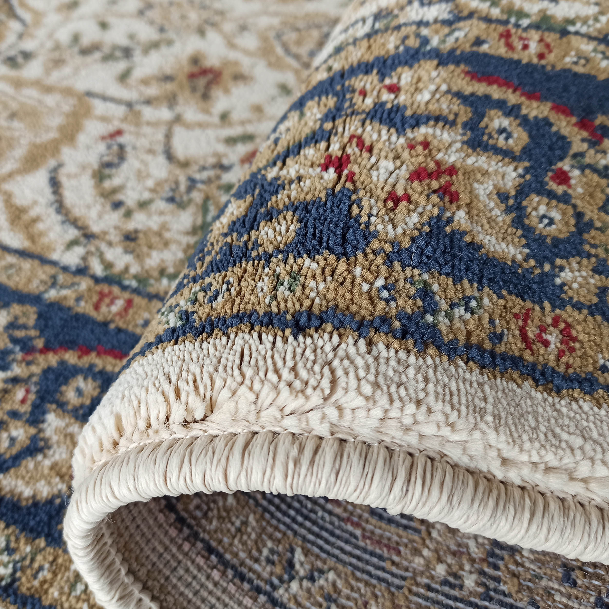 Tapis aux motifs complexes bleus, beiges et rouges, enroulé pour révéler sa texture douce et sa bordure claire