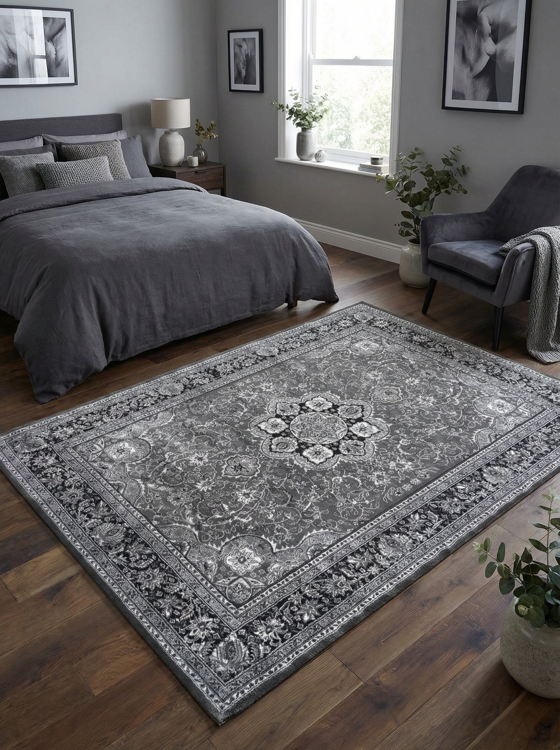 Tapis rectangulaire aux nuances de gris et noir, orné de motifs floraux et d'un médaillon central, sur un parquet de chambre